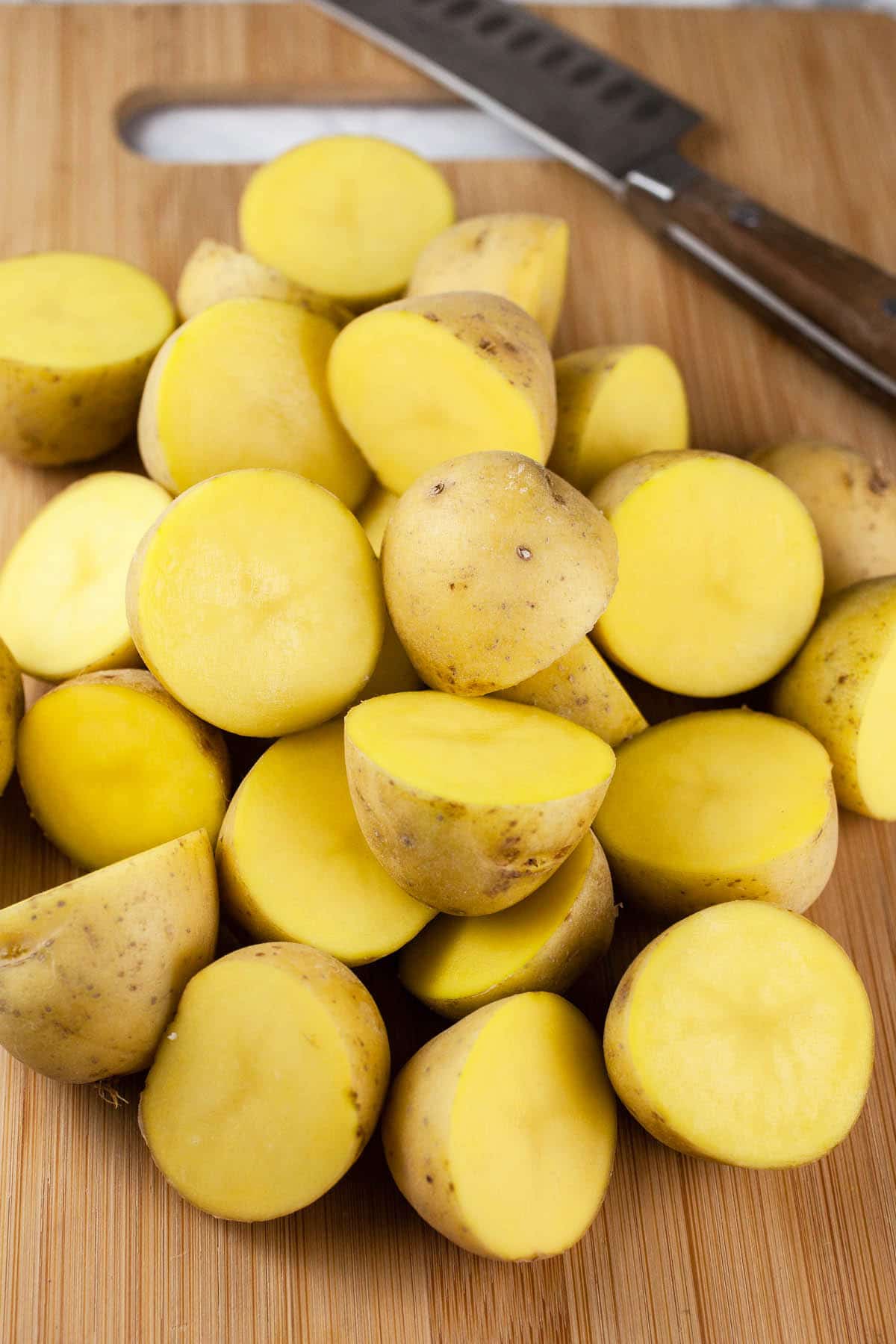 Chopped Yukon gold potatoes on wooden cutting board with knife.