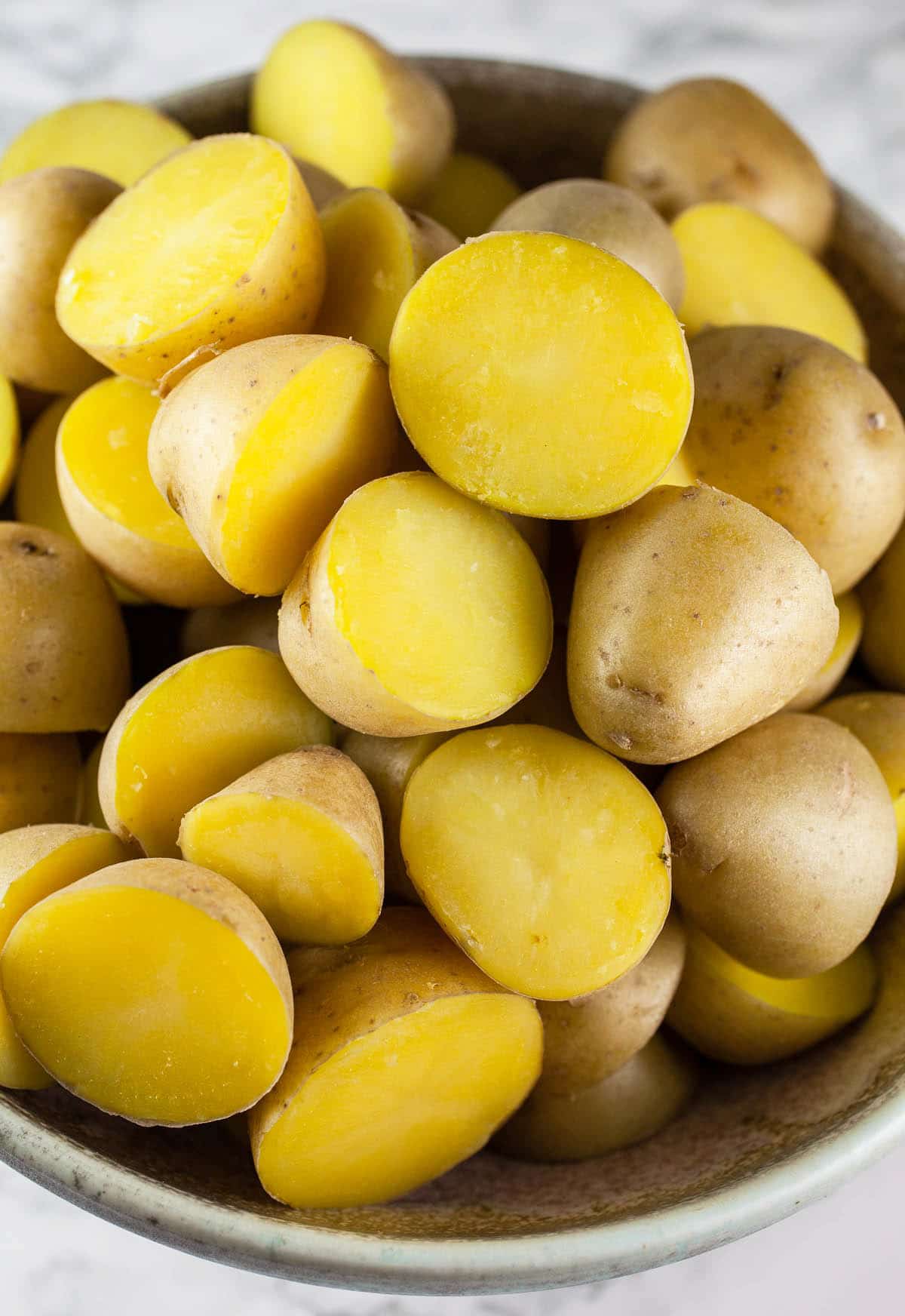 Boiled halved Yukon gold potatoes in ceramic bowl.