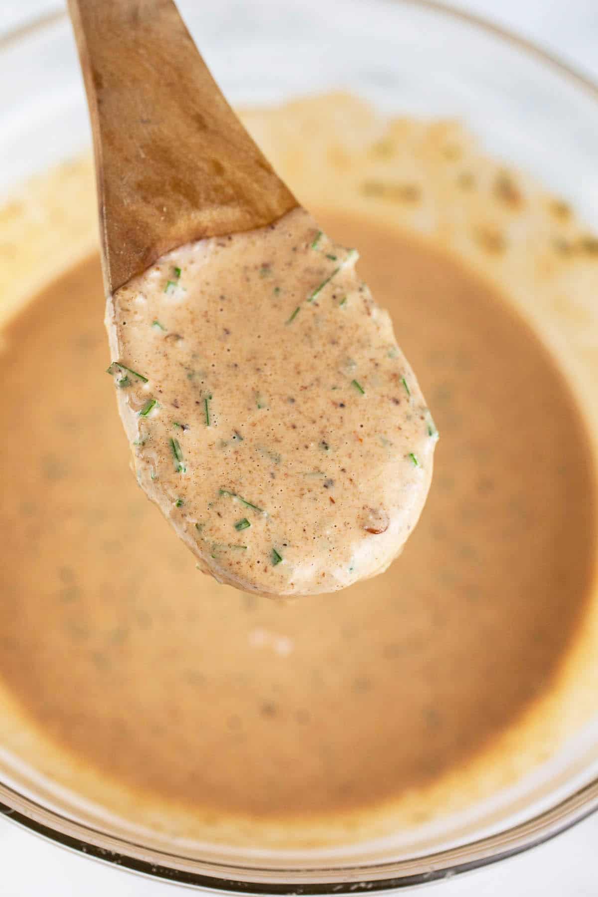 Chipotle mayo dressing on wooden spoon lifted from small glass bowl.