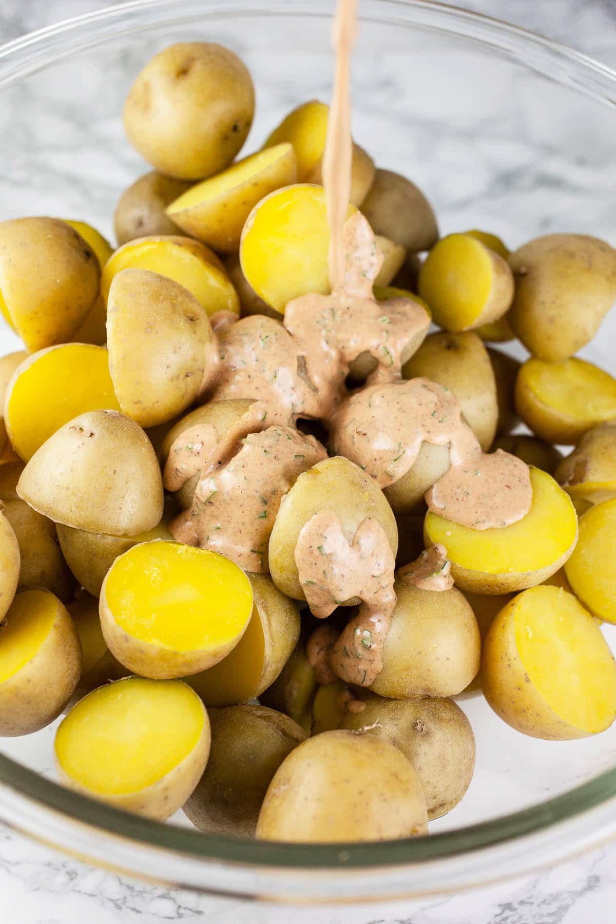 Chipotle mayo dressing poured over cooked Yukon gold potatoes in large glass bowl.