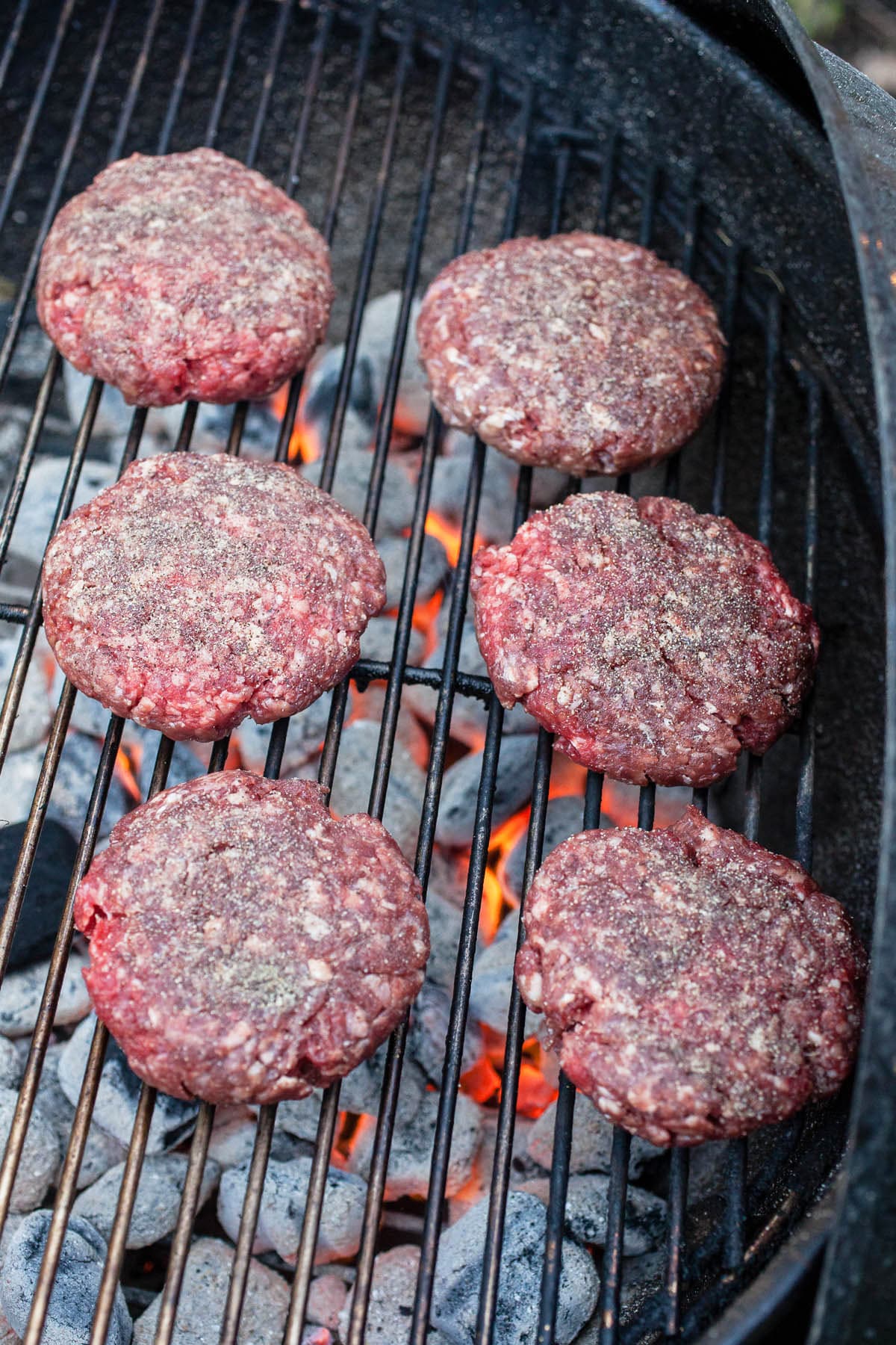 Ground beef patties cooking on Weber charcoal grill.