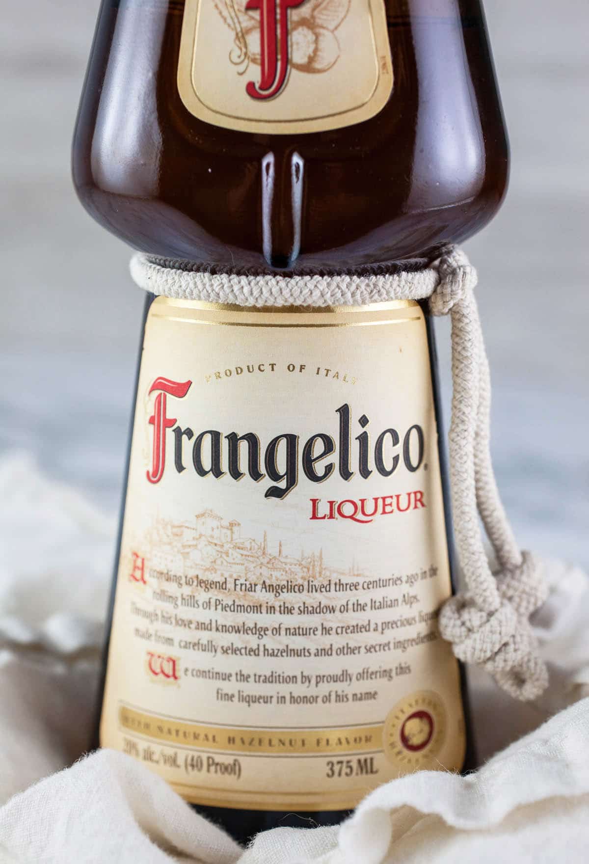This Italian Chocolate Hazelnut Cake recipe is the best simple and authentic dessert! It's easy to make and full of traditional Italian flavors like coffee, chocolate, and hazelnut. This moist cake is flavored with Frangelico liqueur and topped with a homemade chocolate ganache. Learn how to make this cake from scratch. It's one of my favorite sweet treats and perfect with some espresso! #italian #chocolate #hazelnut #cake #desserts #recipes Bottle of Frangelico liqueur on white cloth.