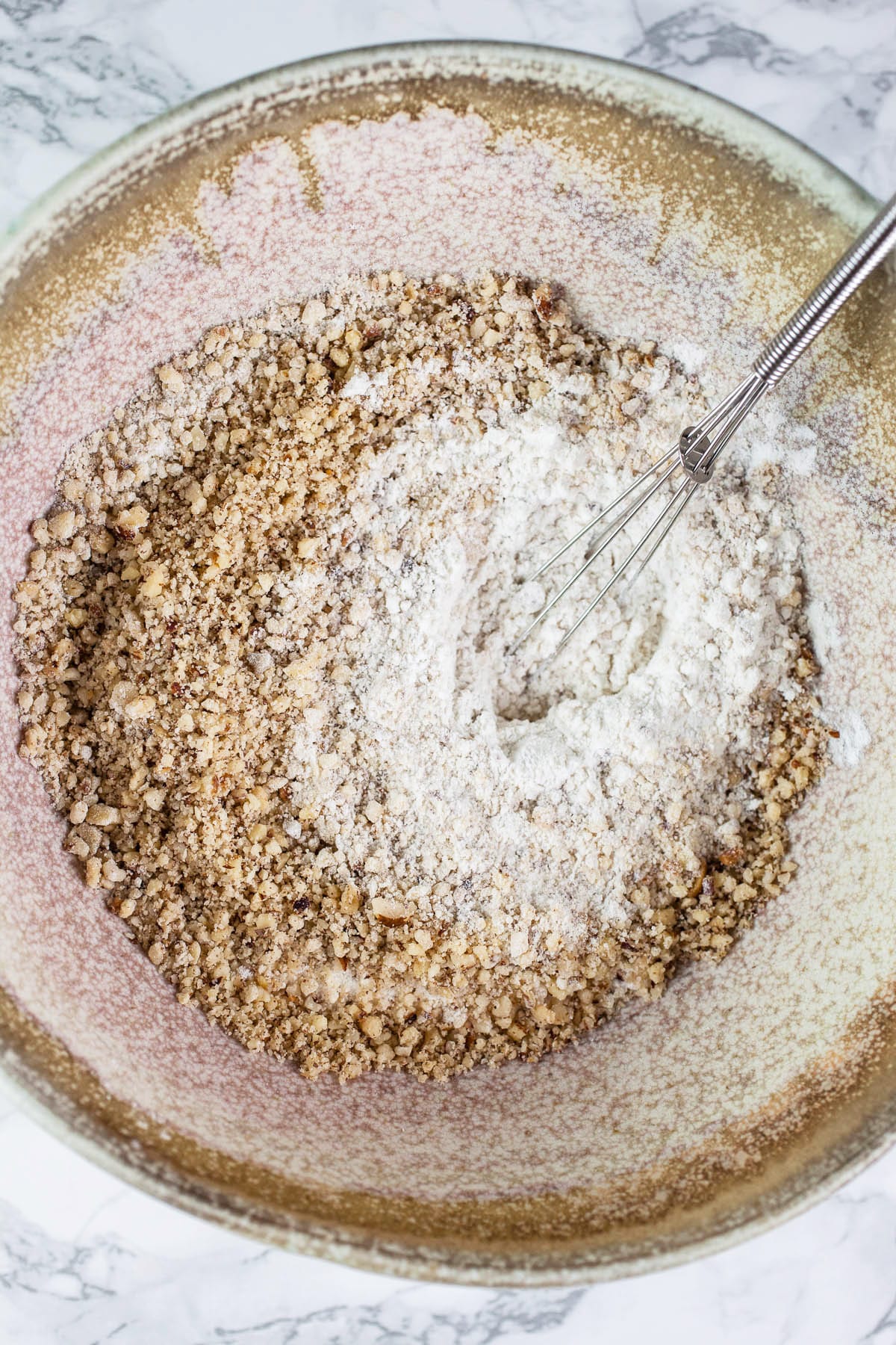 Dry ingredients and ground hazelnuts in ceramic bowl.