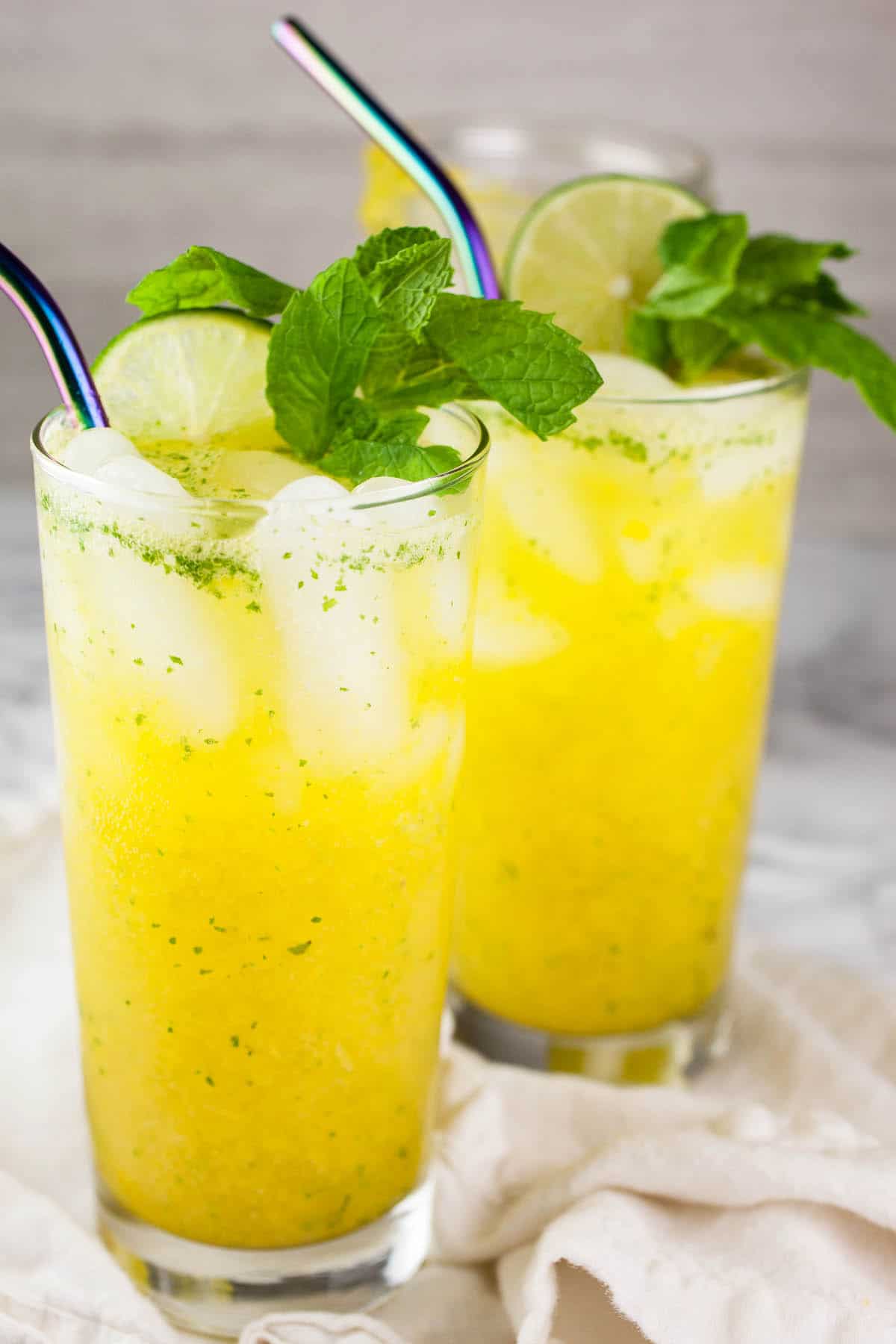 Mango mojito mocktails in tall glasses with mint and lime.