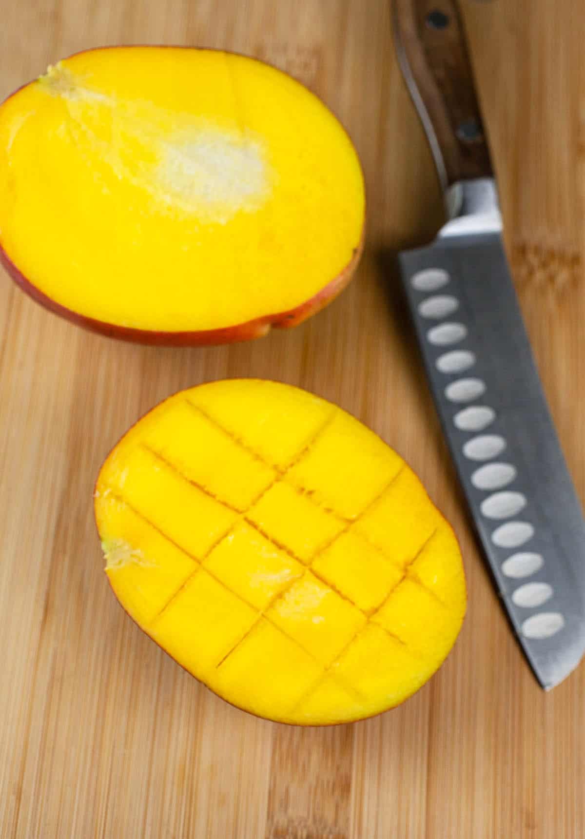 Mango cut in half on wooden cutting board with knife.