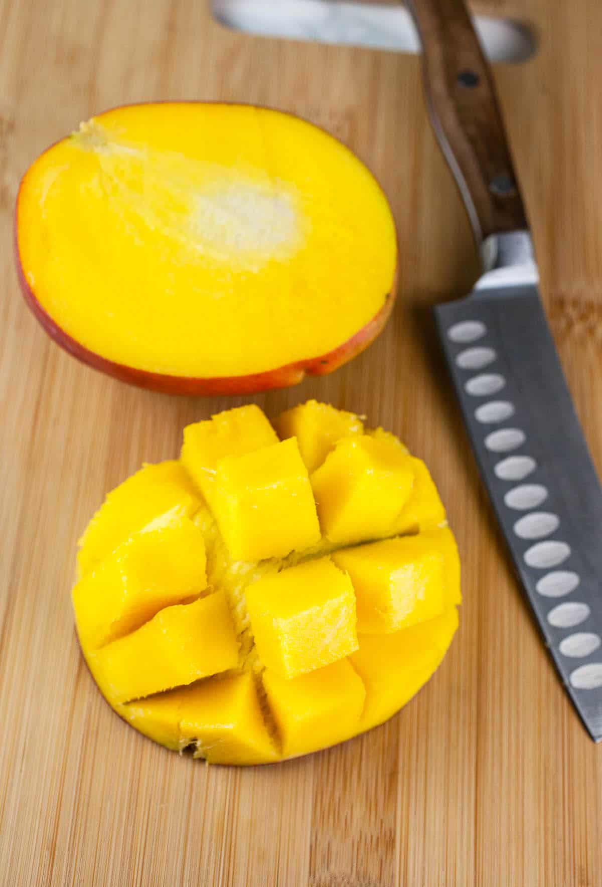 Mango cut in half and fanned out on wooden cutting board with knife.