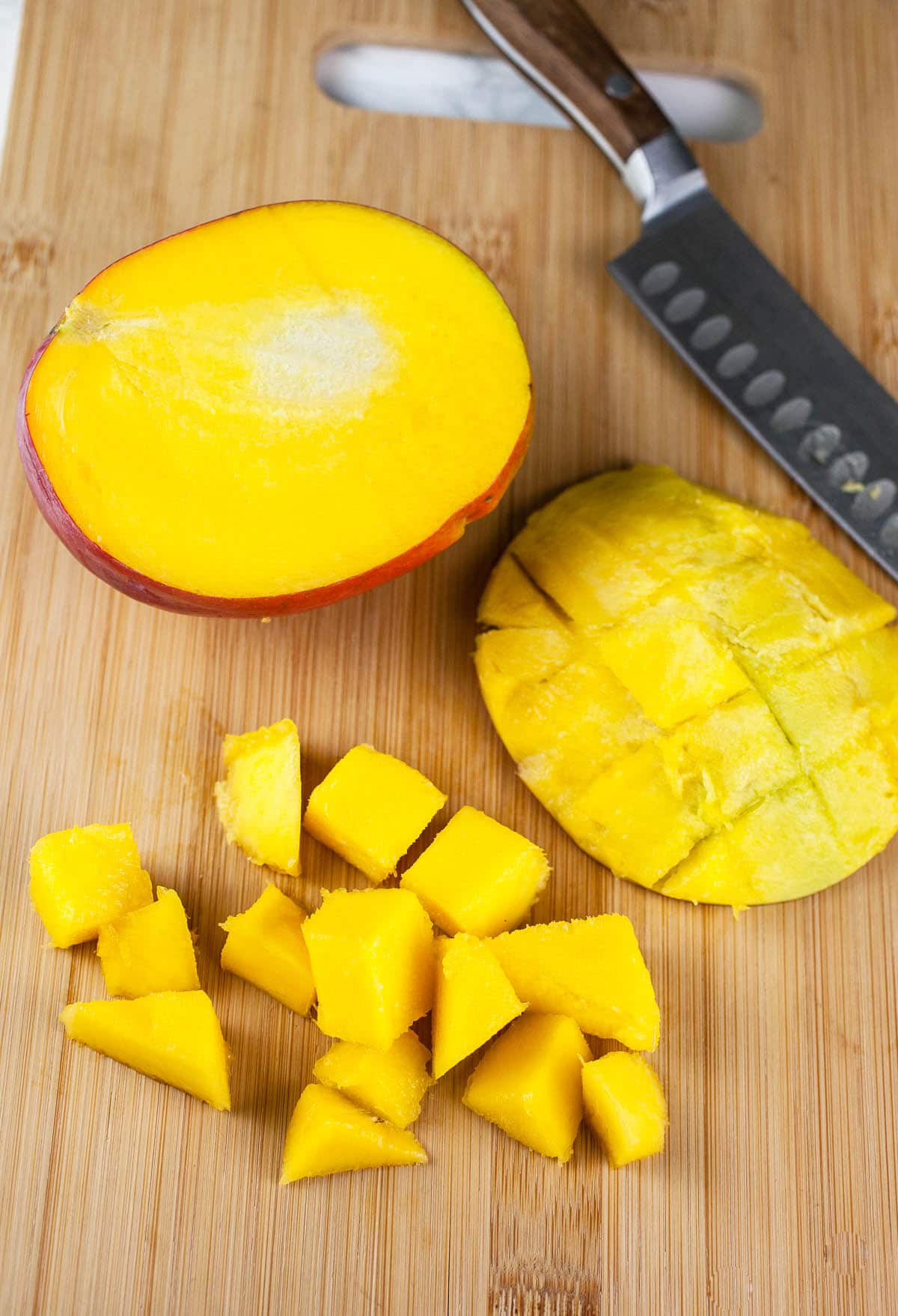 Mango cut into chunks on wooden cutting board with knife.