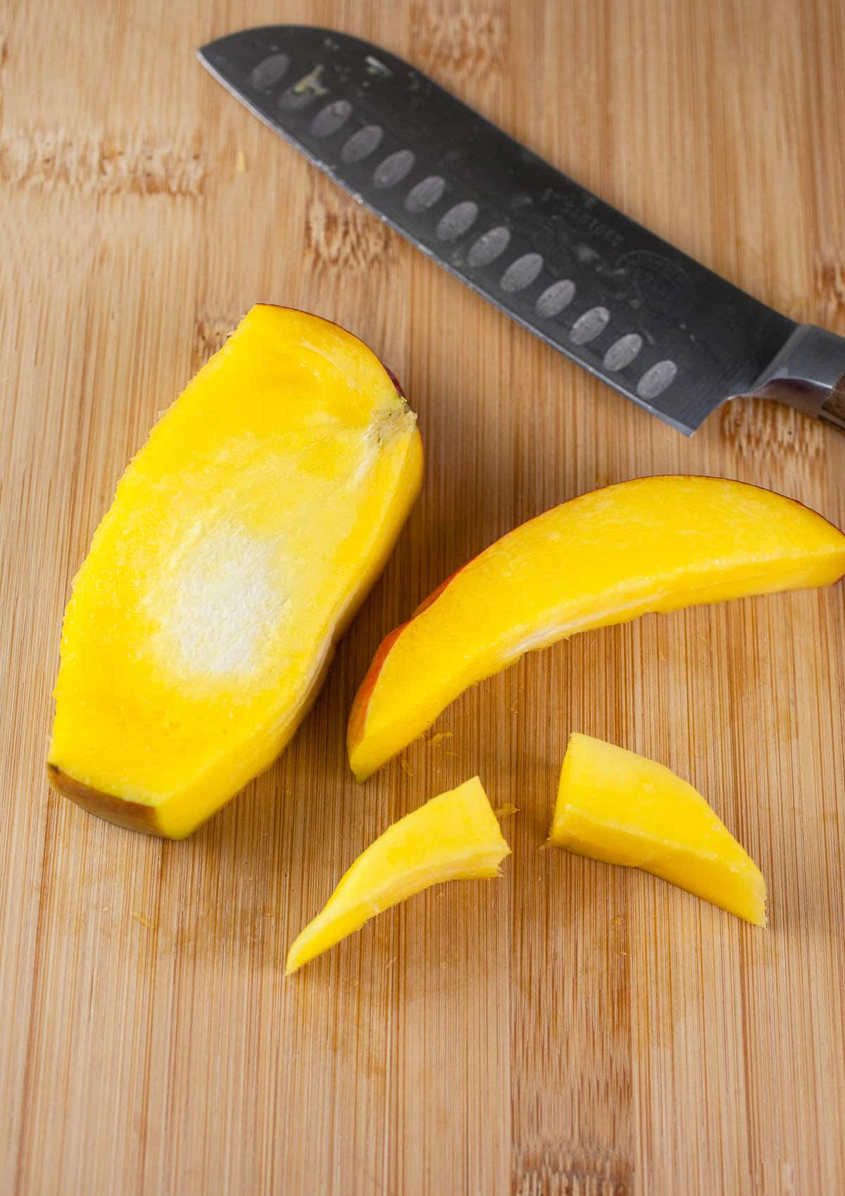 Sides of mango cut from fruit on wooden cutting board with knife.