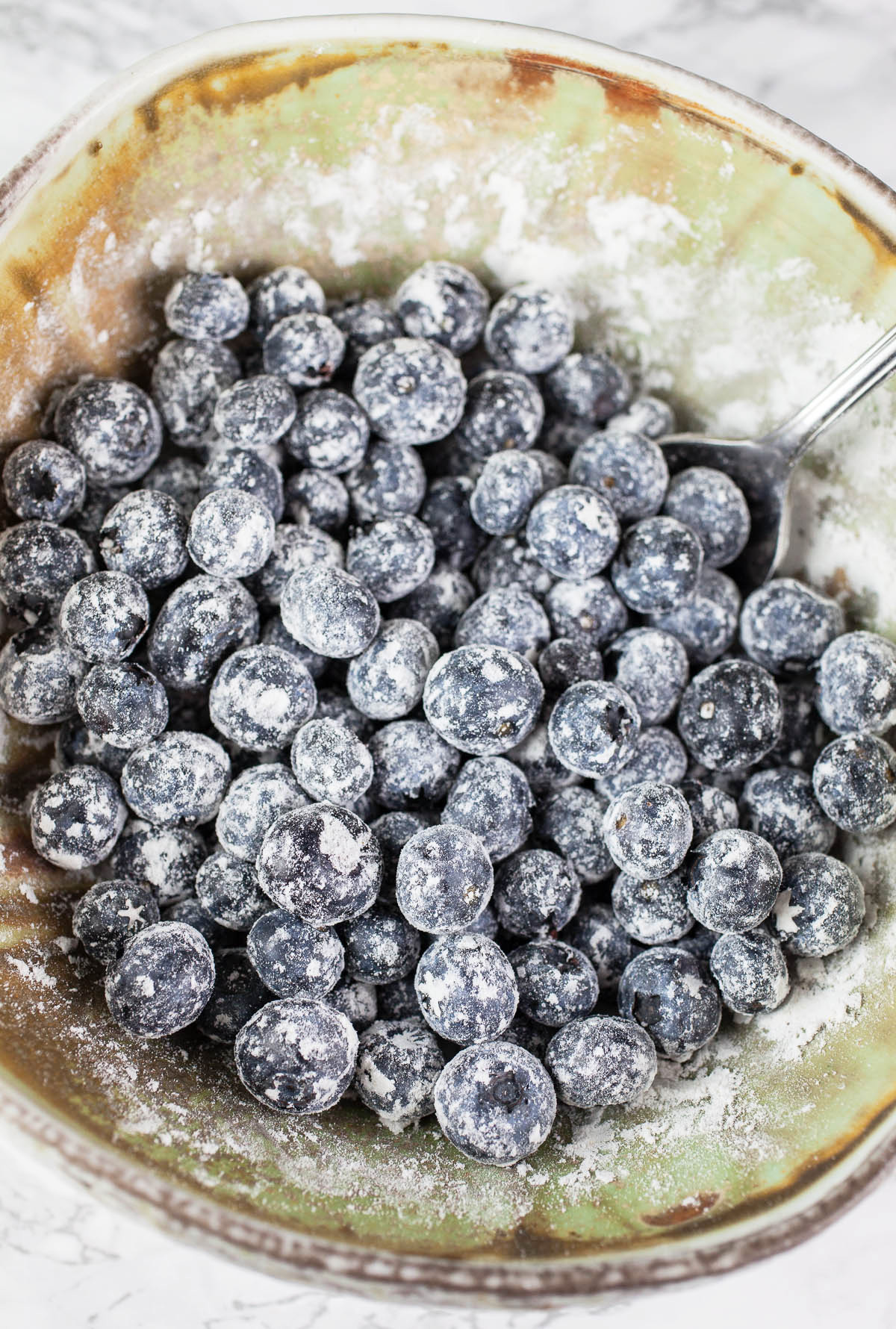 Fresh blueberries tossed in flour in ceramic bowl.