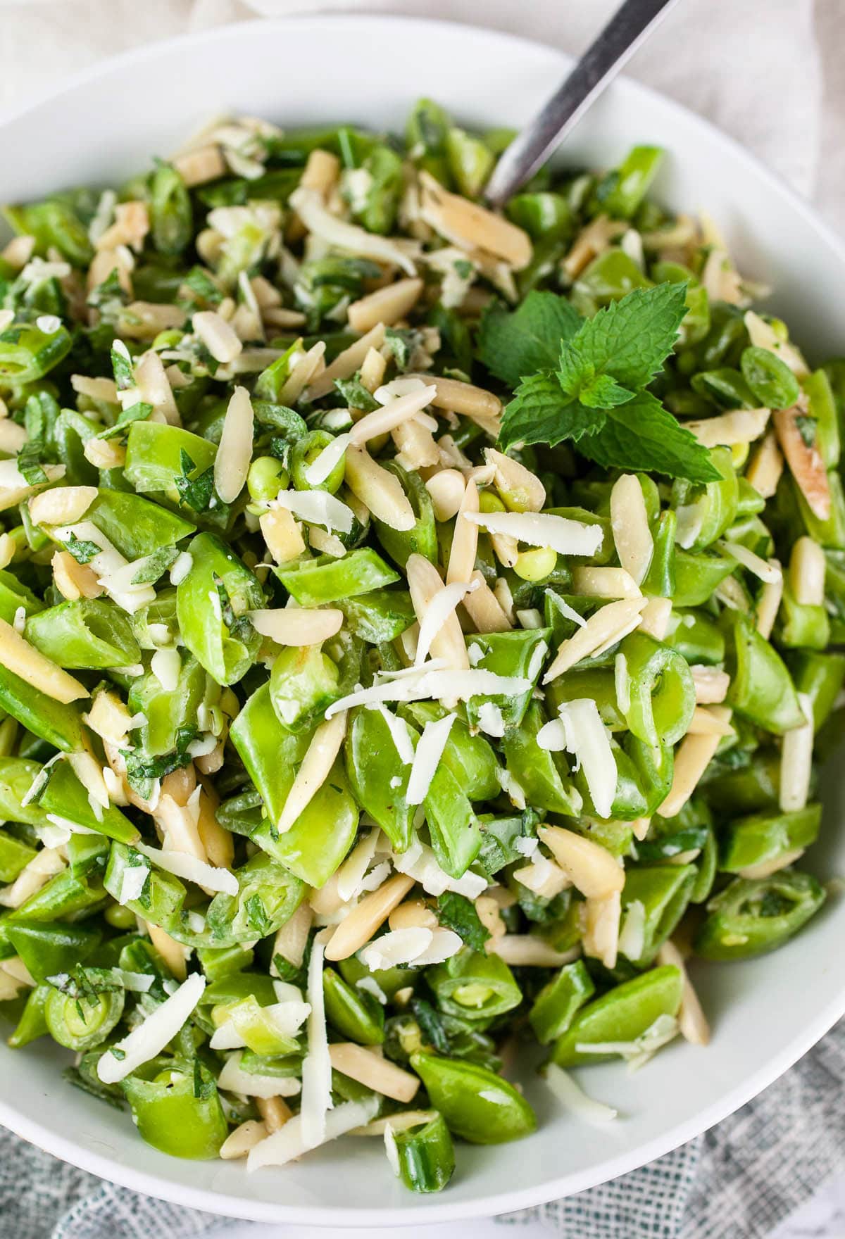 Pea salad with mint, almonds, and Parmesan cheese in white bowl.