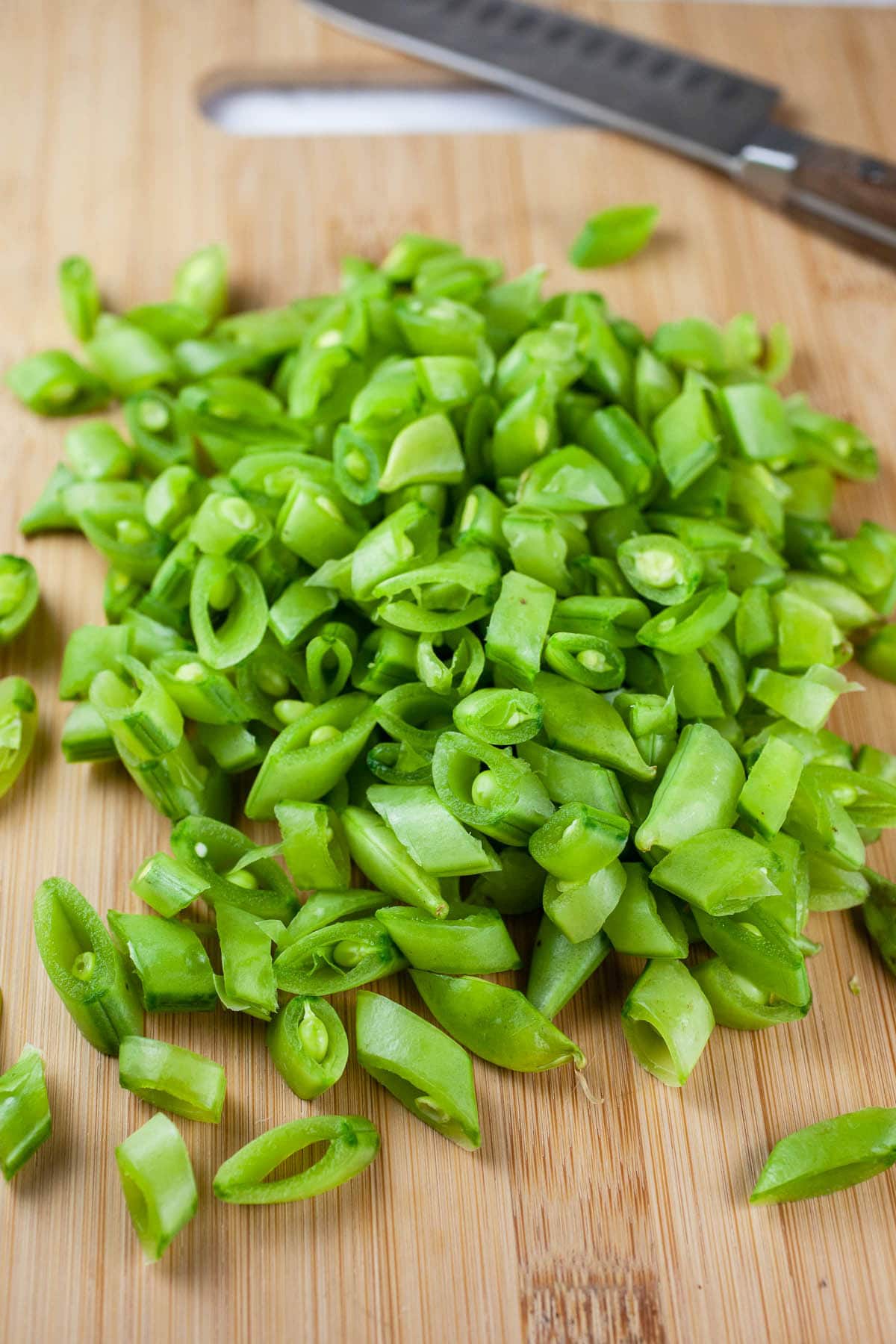 Chopped snap peas on wooden cutting board with knife.