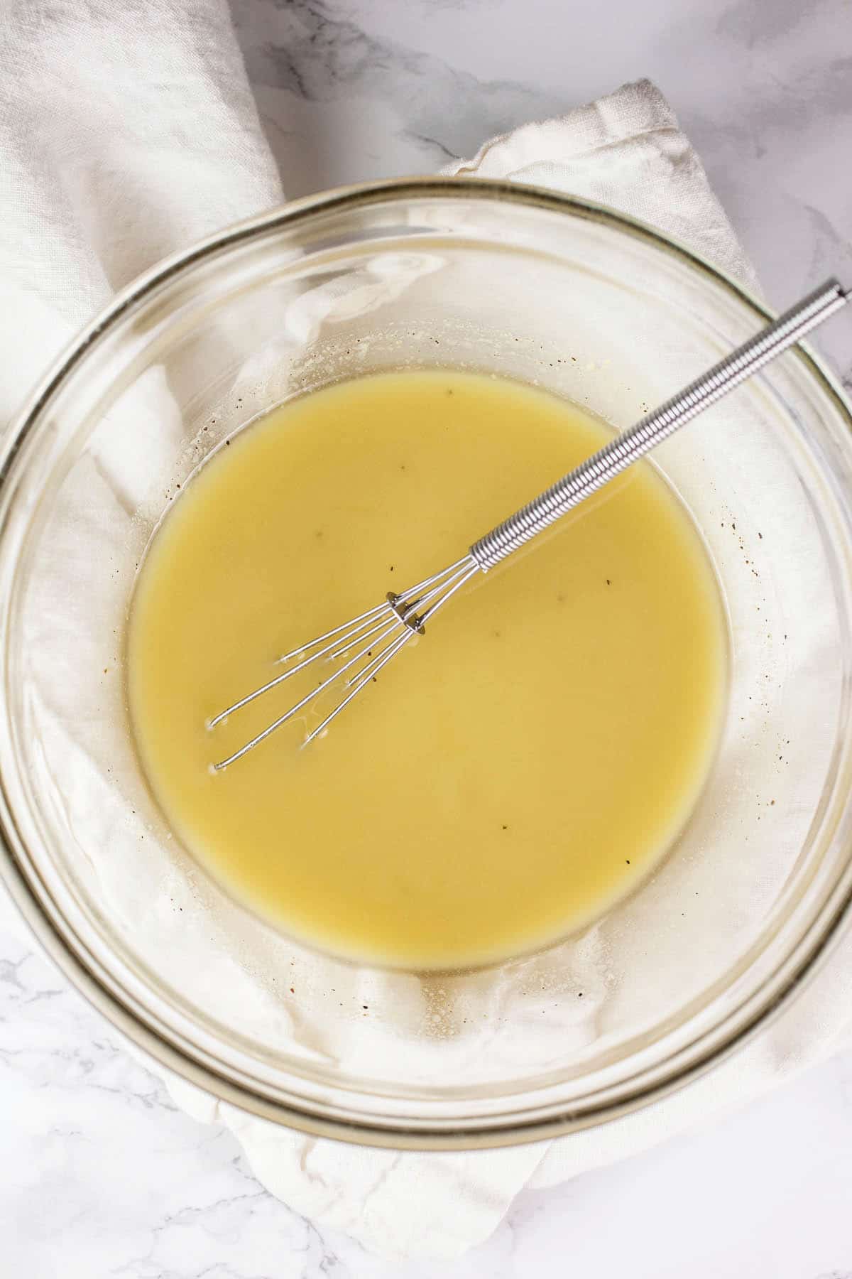 Salad dressing in small glass bowl with whisk.