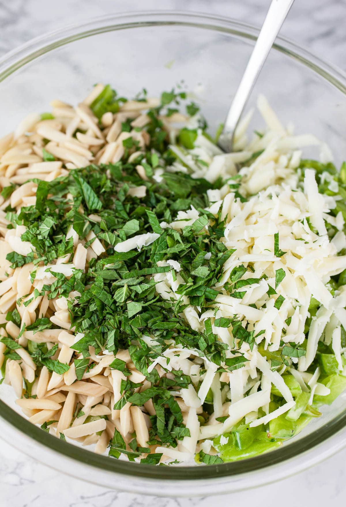 Chopped peas, toasted almonds, mint, and Parmesan cheese in large glass mixing bowl.