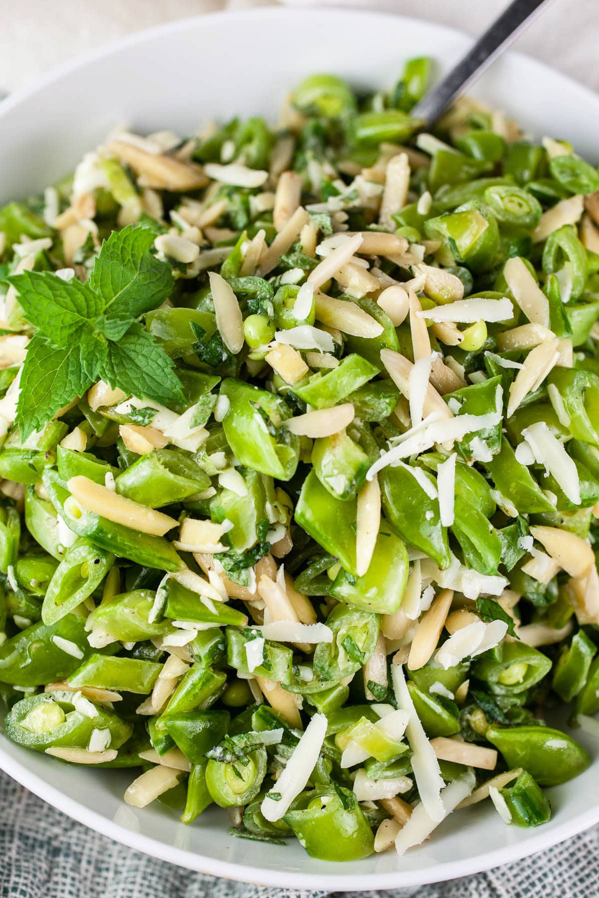 Healthy pea mint salad with almonds and Parmesan cheese in white bowl.