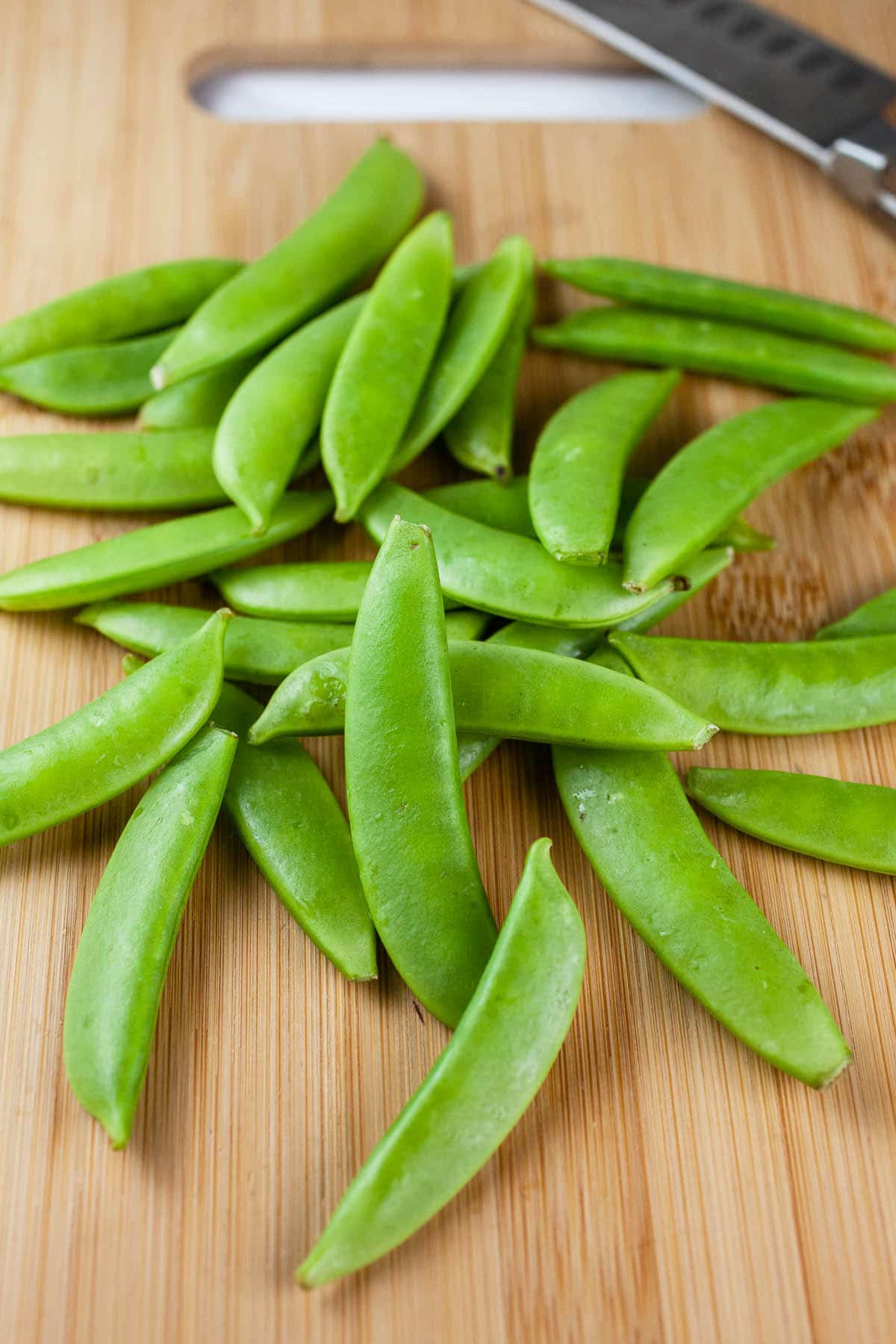 Snap peas on wooden cutting board with knife.