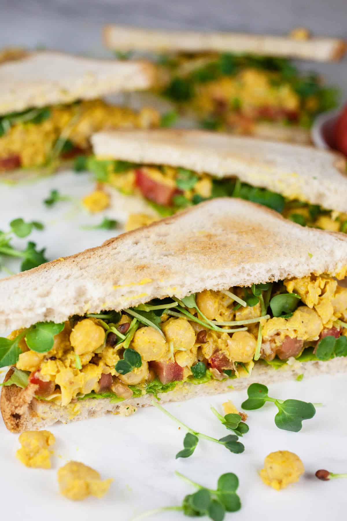 Curried chickpea salad sandwiches cut into halves.