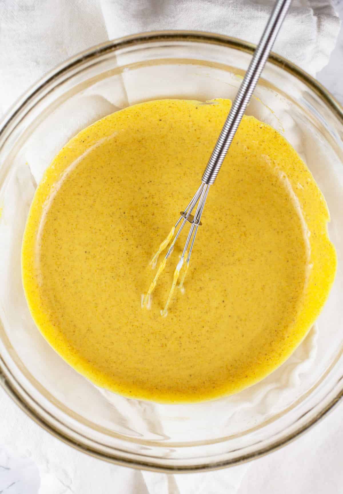 Curry vegan mayo dressing in small glass bowl with whisk.