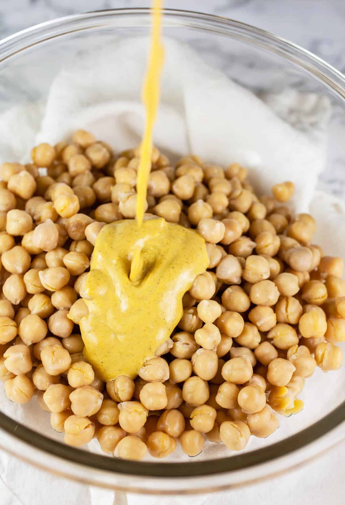 Vegan curry mayo dressing poured into large glass bowl of chickpeas.