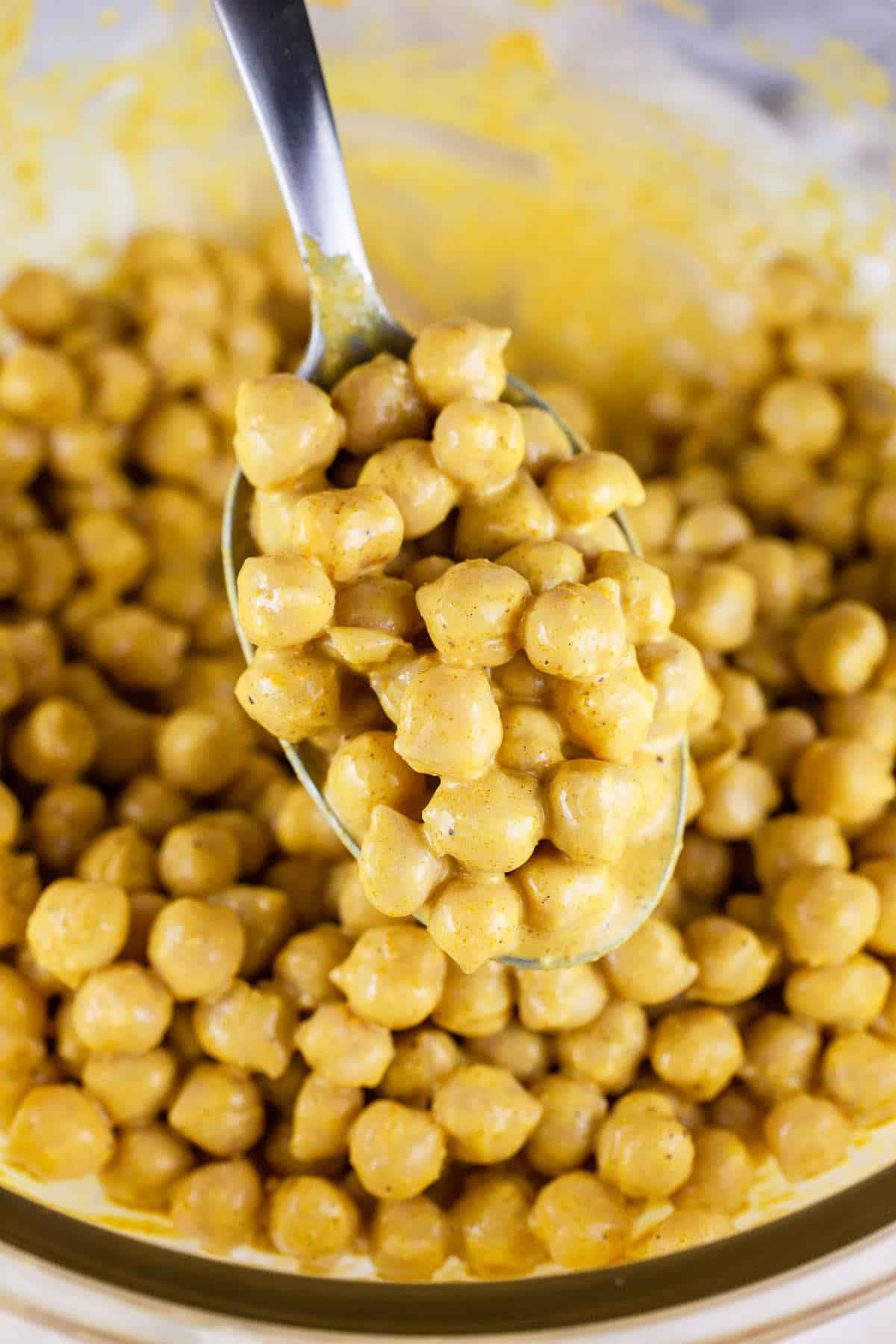 Spoonful of curry chickpea salad lifted from glass bowl.