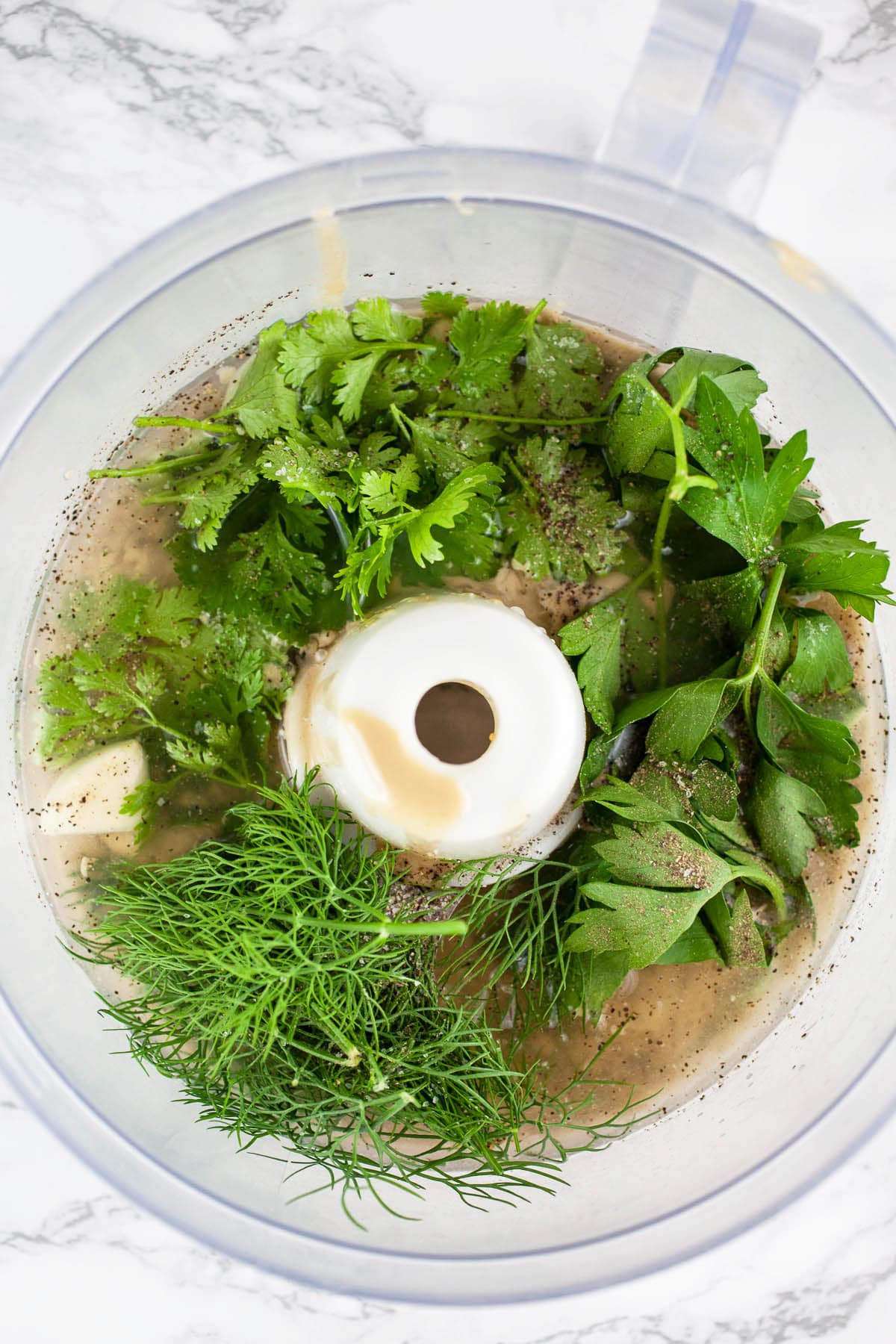 Tahini paste, lemon juice, water, garlic, and fresh herbs in food processor.