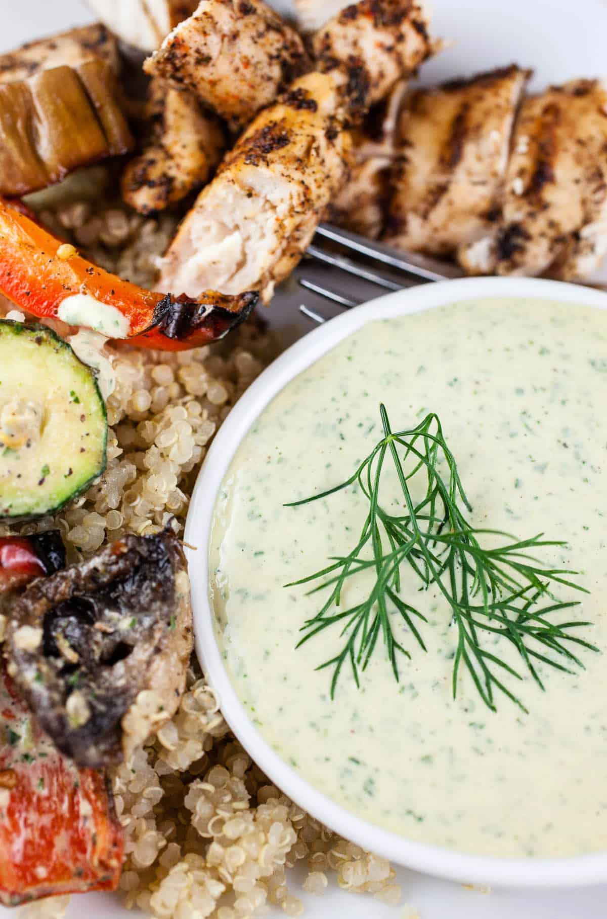 Lemon herb tahini sauce in small white bowl with grilled chicken and vegetables.
