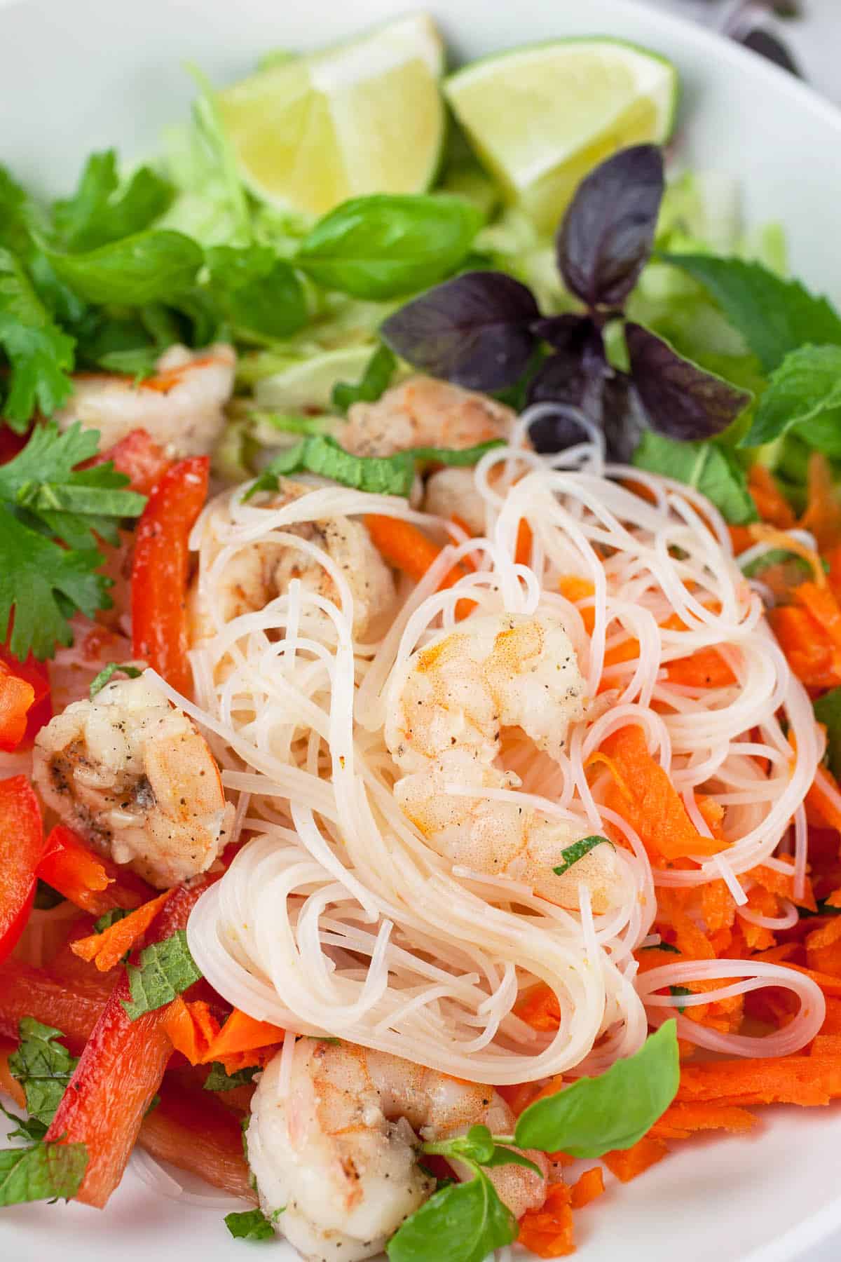 Vietnamese noodle salad with shrimp, veggies, and herbs in white bowl.
