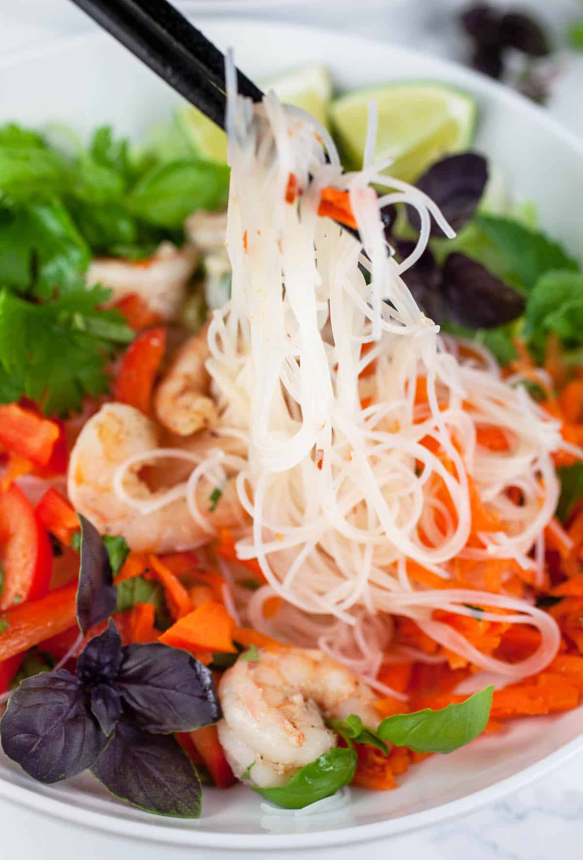 Vietnamese noodle salad lifted from white bowl with chopsticks.