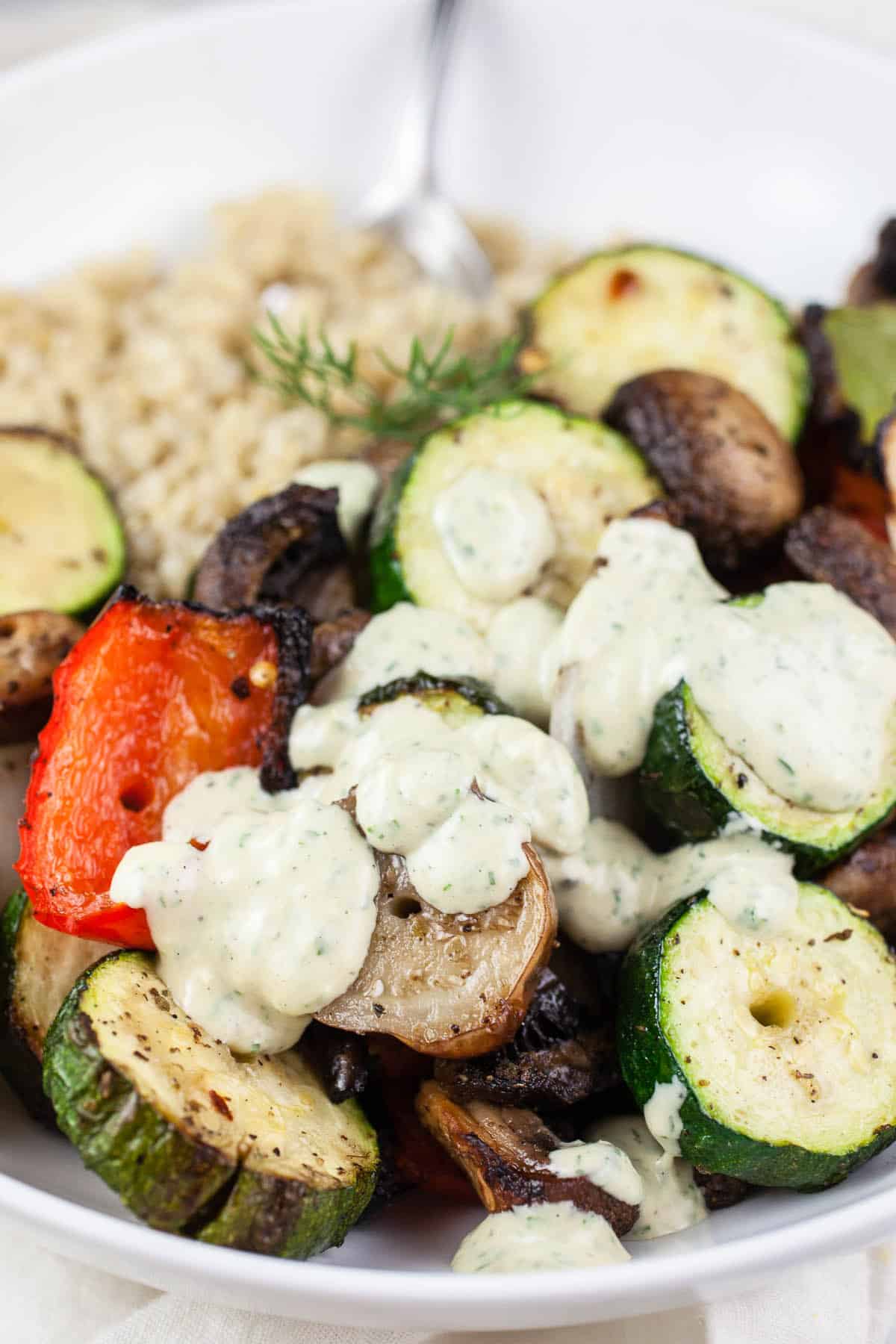 Tahini sauce on top of grilled vegetables and quinoa in white bowl.