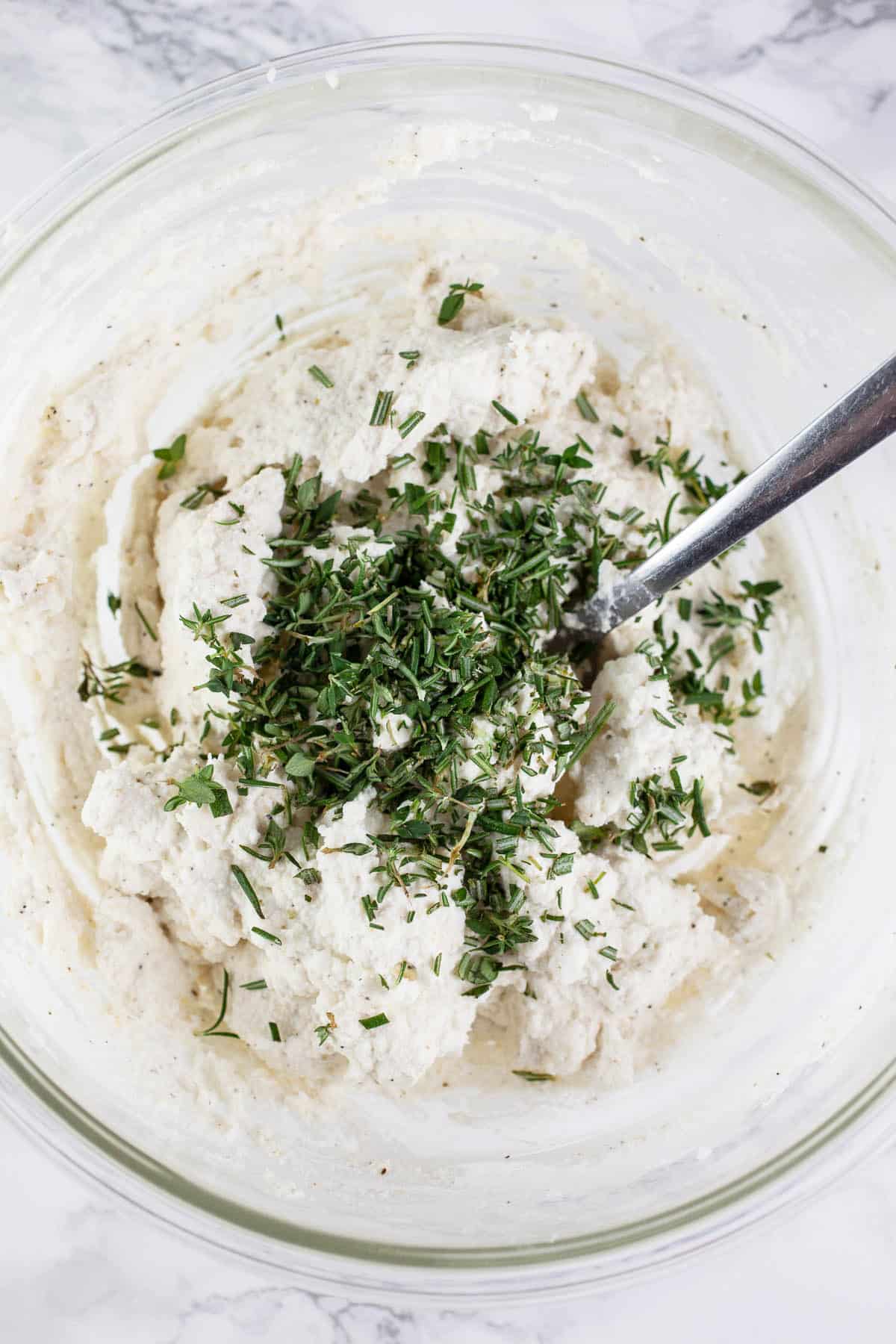 Ricotta feta cheese herb mixture in small glass bowl with fork.