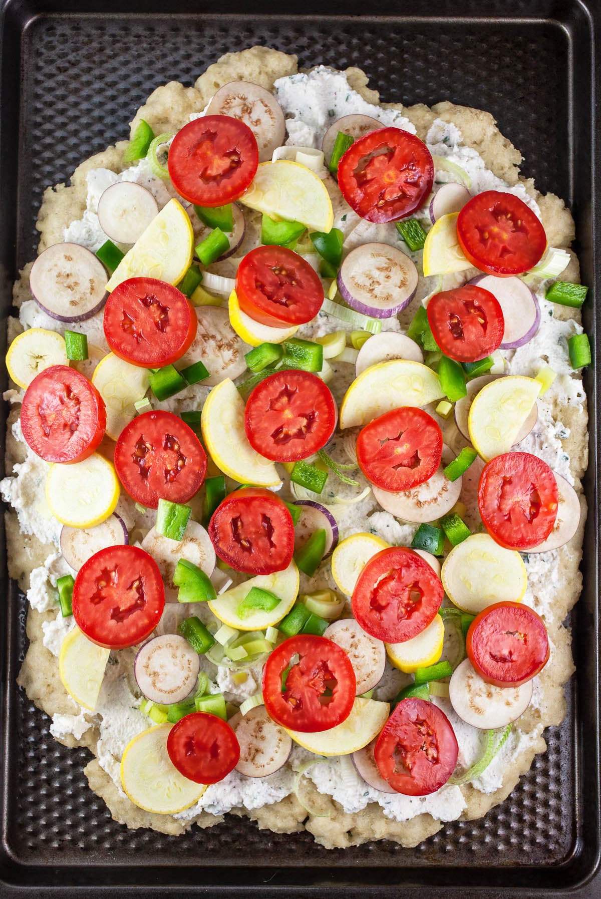 Ricotta cheese spread and chopped vegetables on parbaked pizza crust.