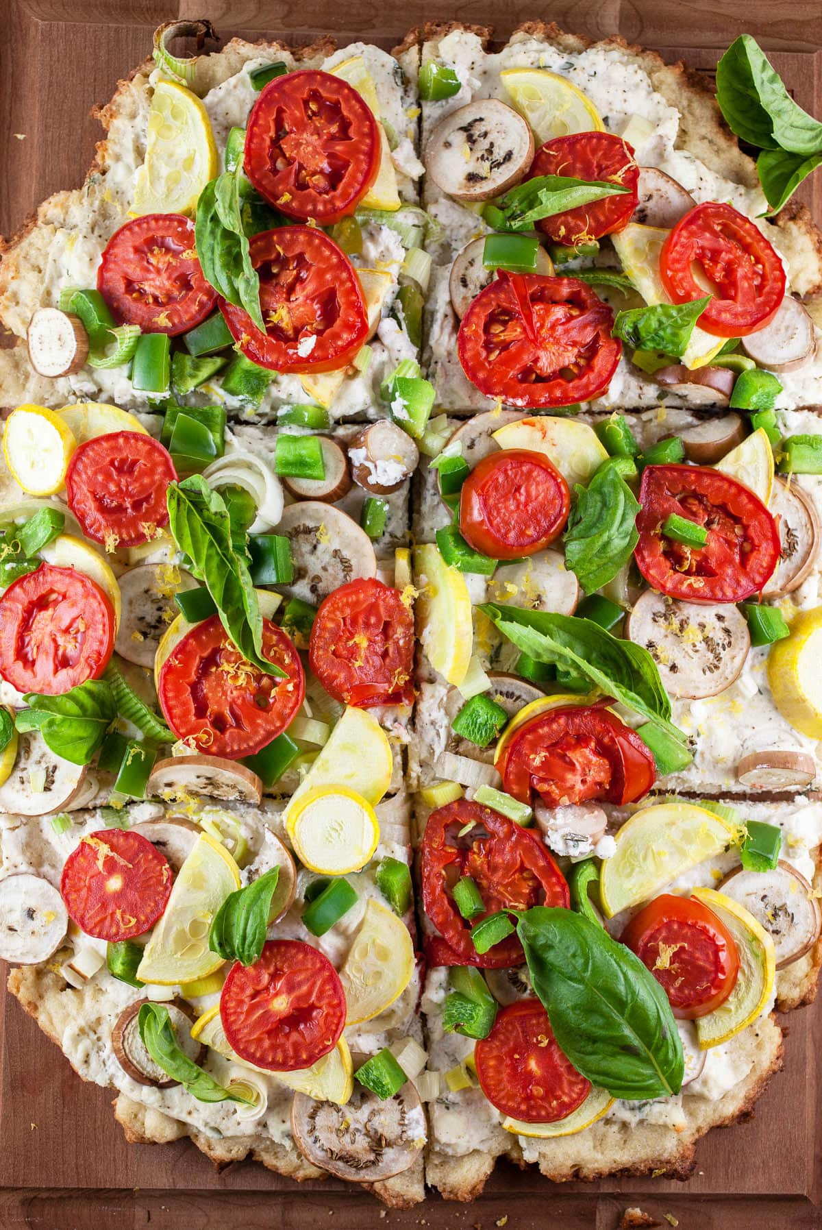 Baked farmers market pizza on wooden cutting board cut into slices.