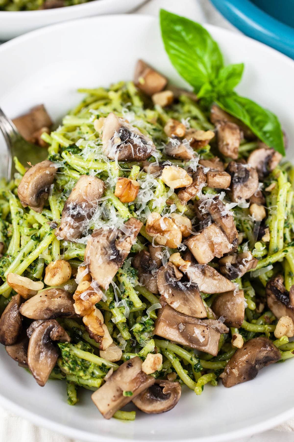 Spinach walnut pesto tossed pasta with sautéed mushrooms in white bowl.