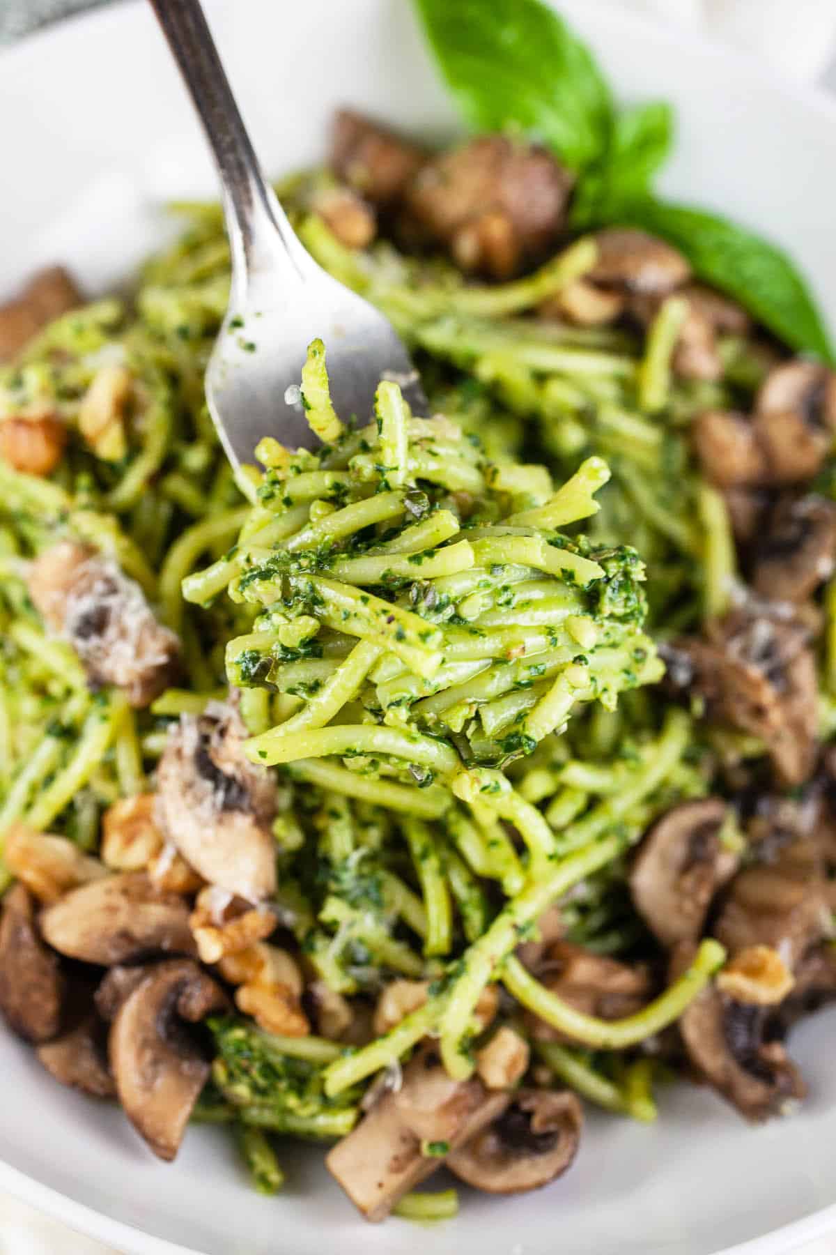 Forkful of spinach walnut pesto pasta lifted from white bowl.
