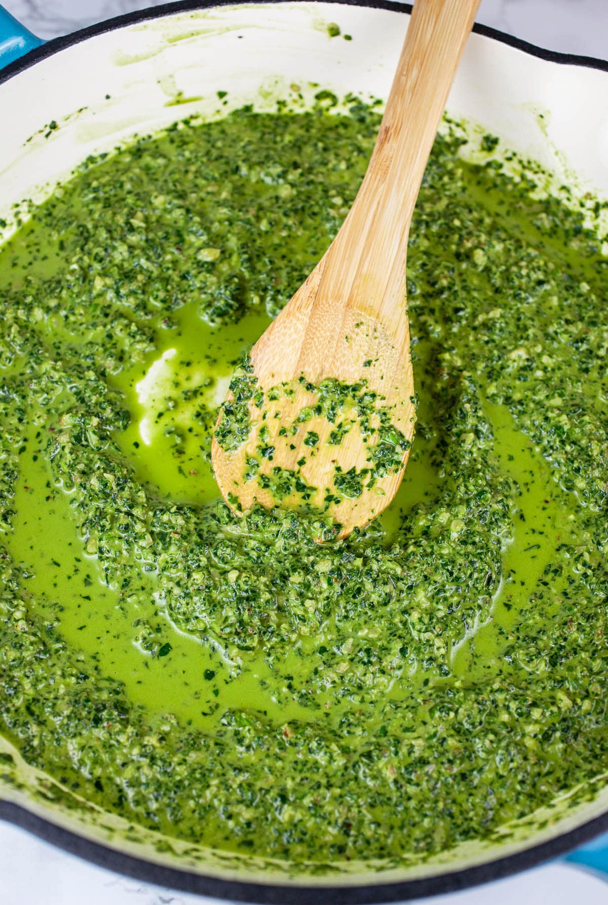 Spinach pesto sauce in skillet with wooden spoon.
