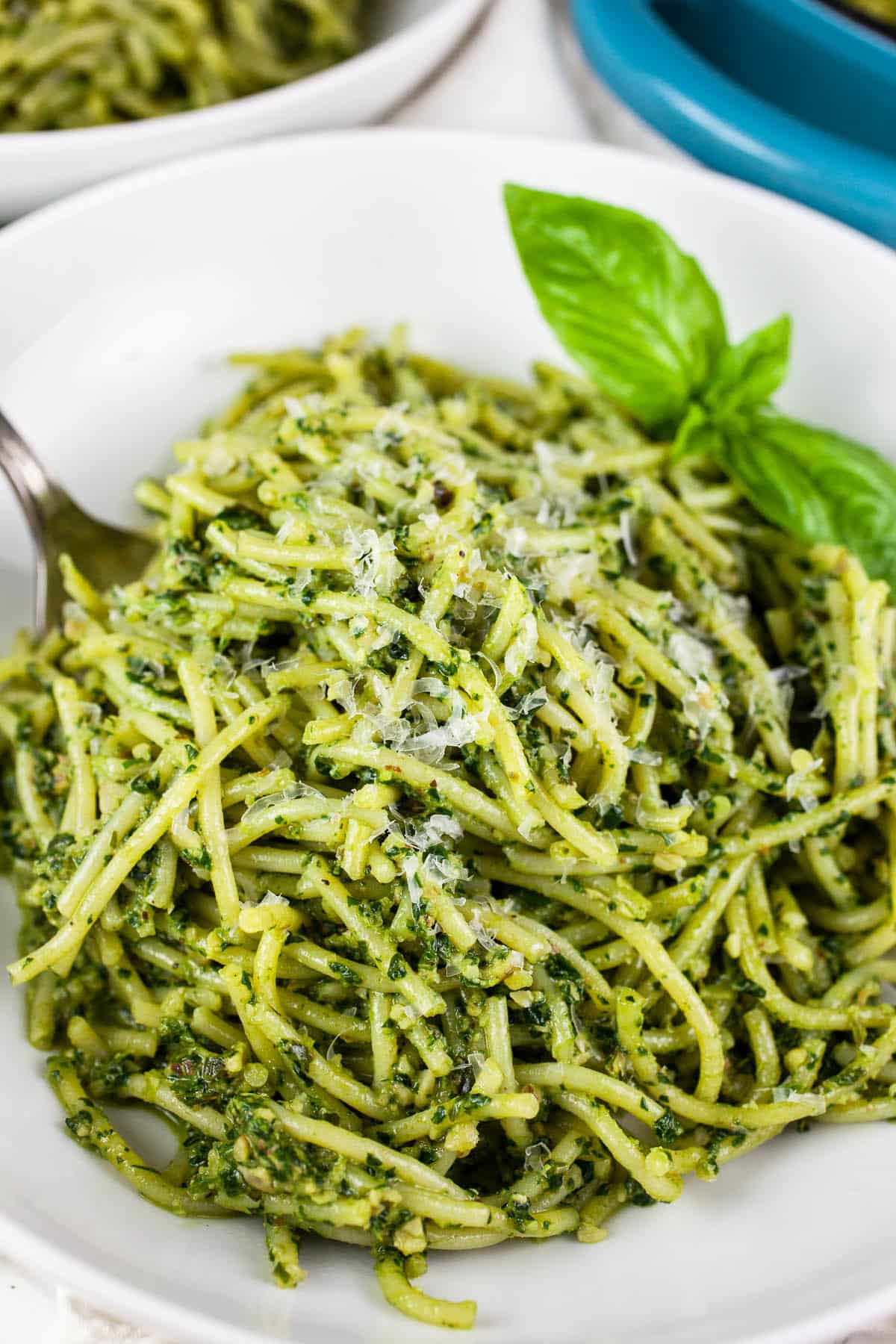 Spinach pesto pasta in white bowl with basil.