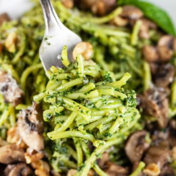 Forkful of spinach walnut pesto pasta lifted from bowl.
