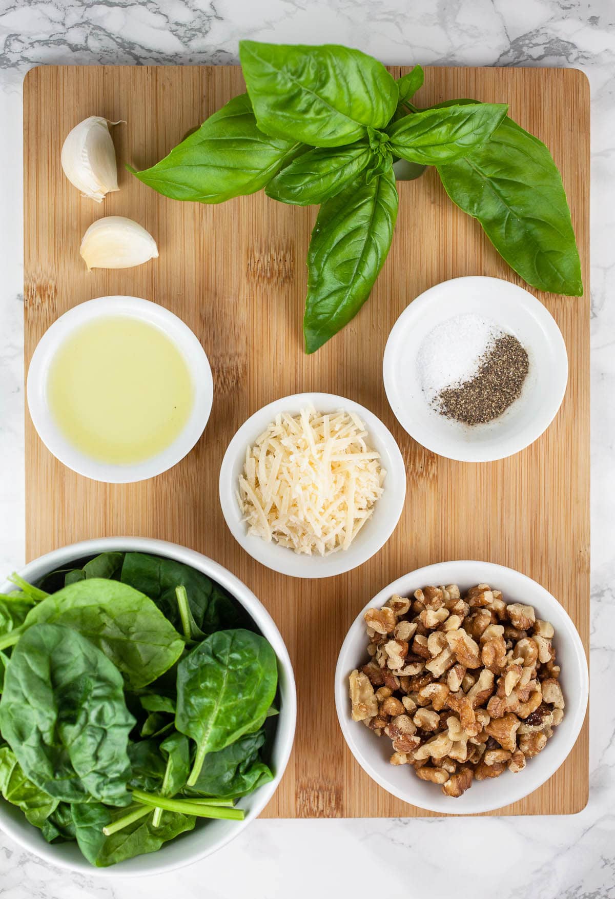 Spinach, walnuts, Parmesan cheese, olive oil, garlic, basil, salt, and pepper on wooden cutting board.