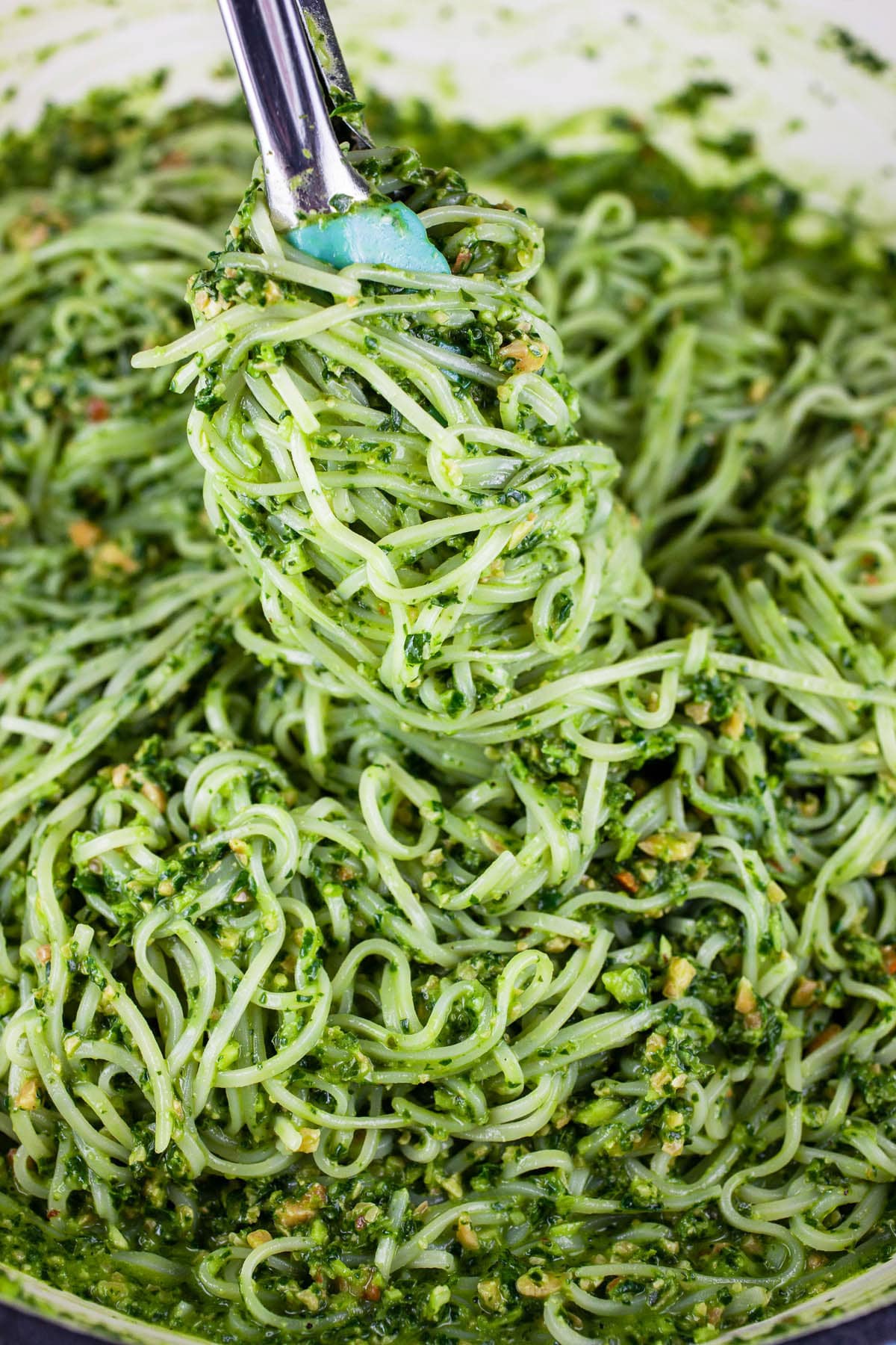 Pesto coated noodles lifted from skillet with tongs.