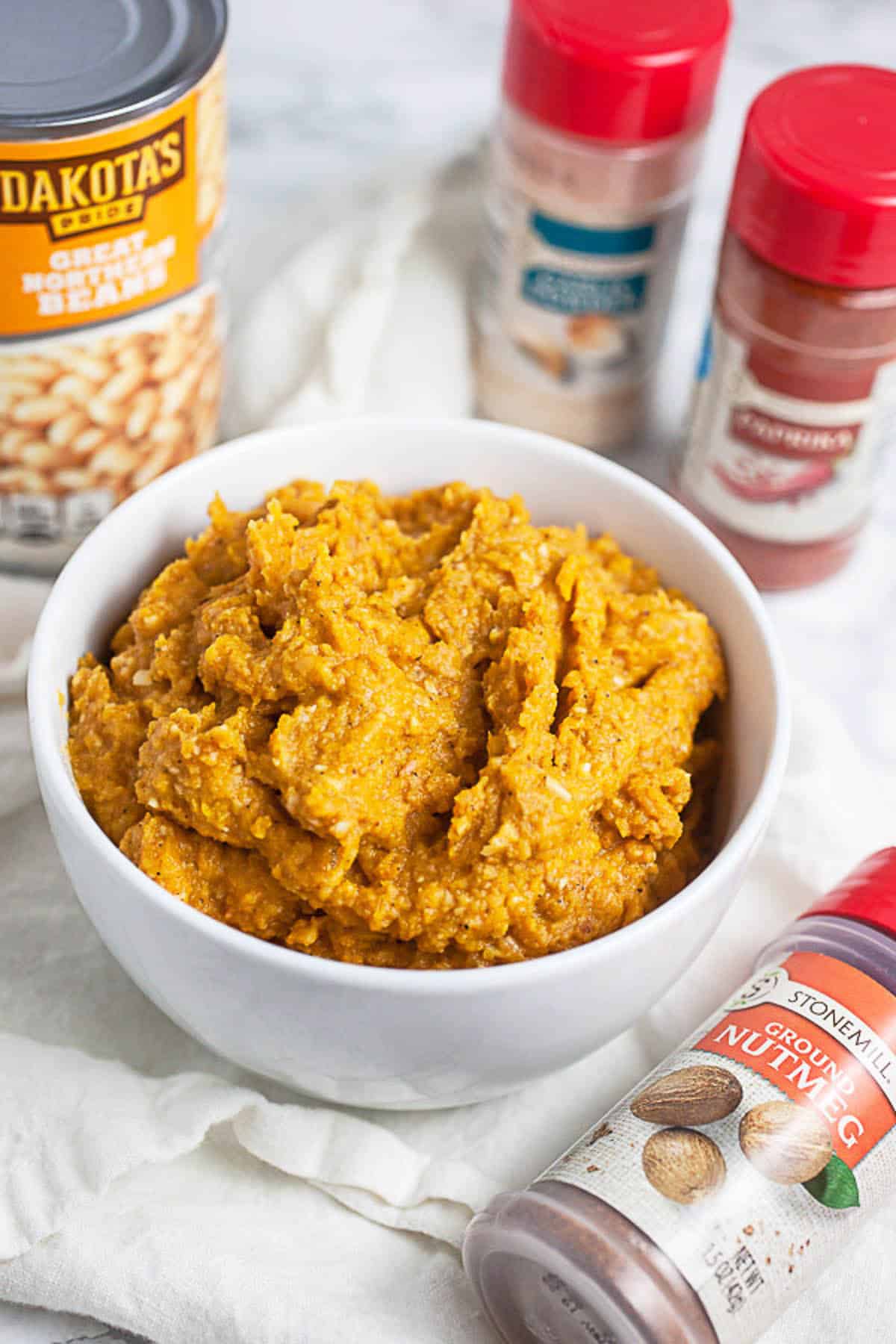 Squash dip in small white bowl next to spices.