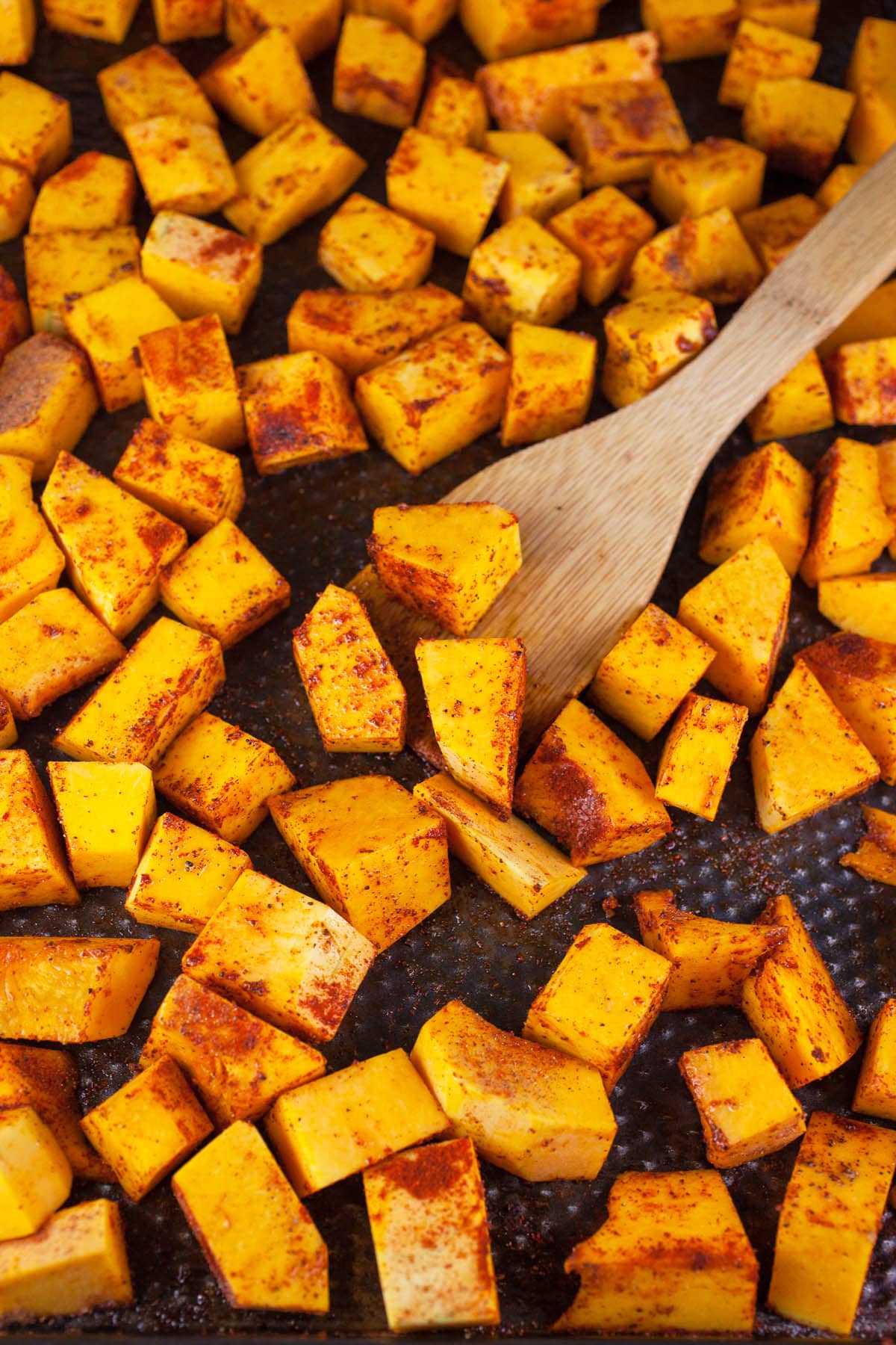 Butternut squash chunks in olive oil and spices on baking sheet.