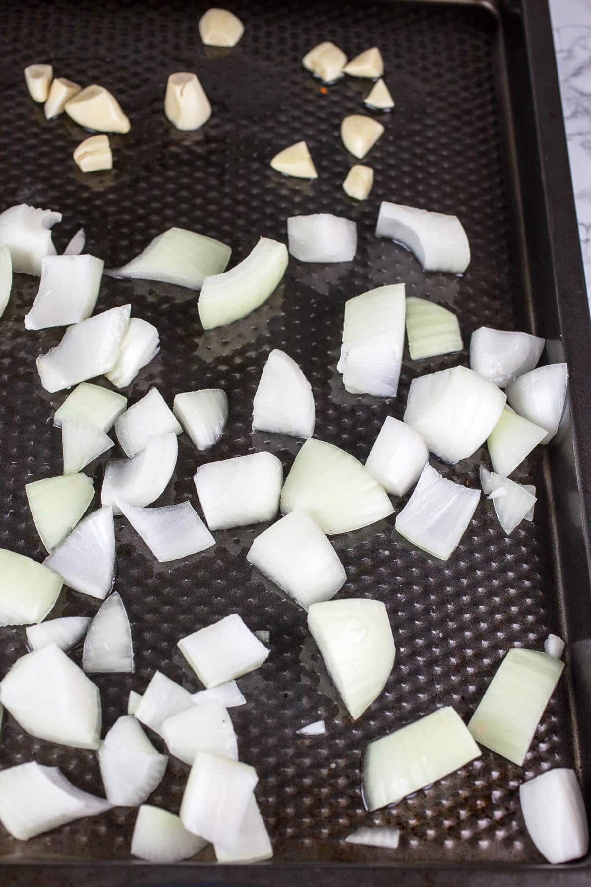 Garlic and onion chunks in olive oil on baking sheet.