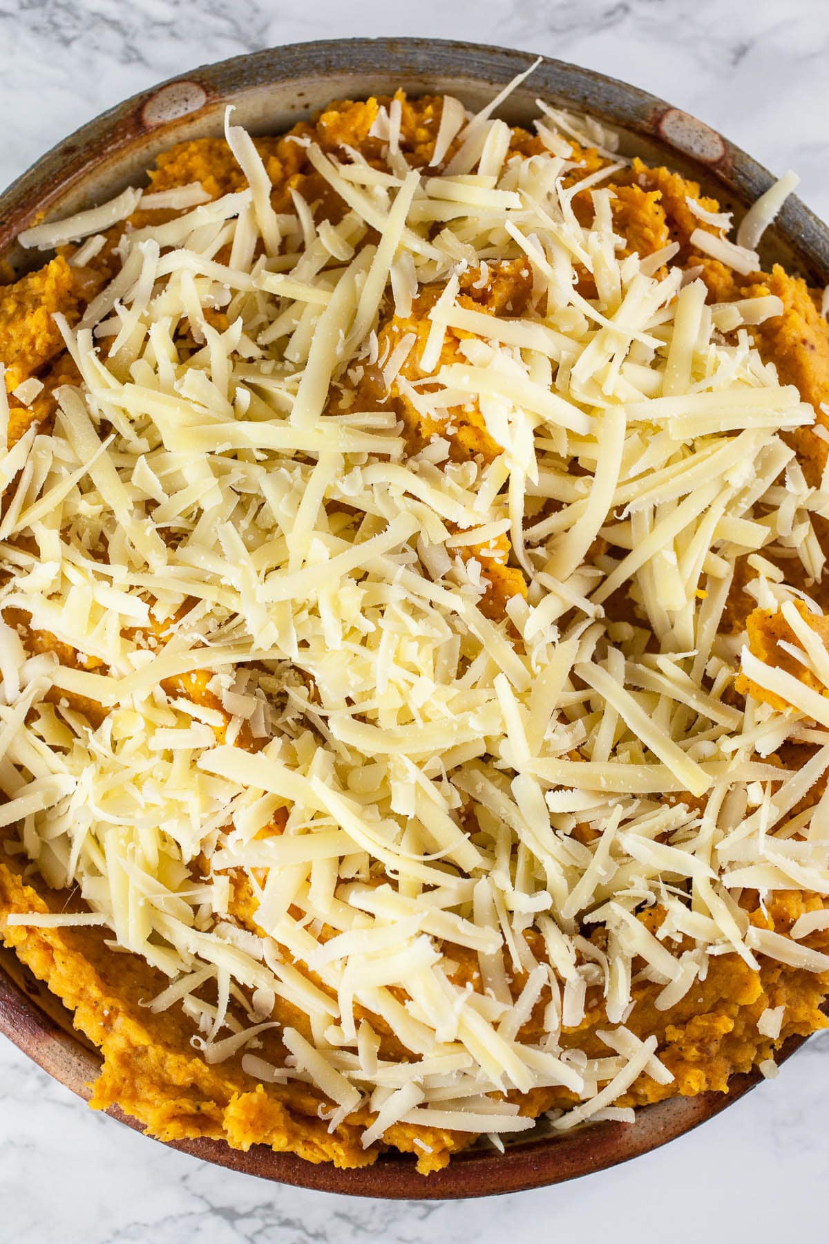 Shredded Gruyere cheese on butternut squash dip in ceramic pie plate.