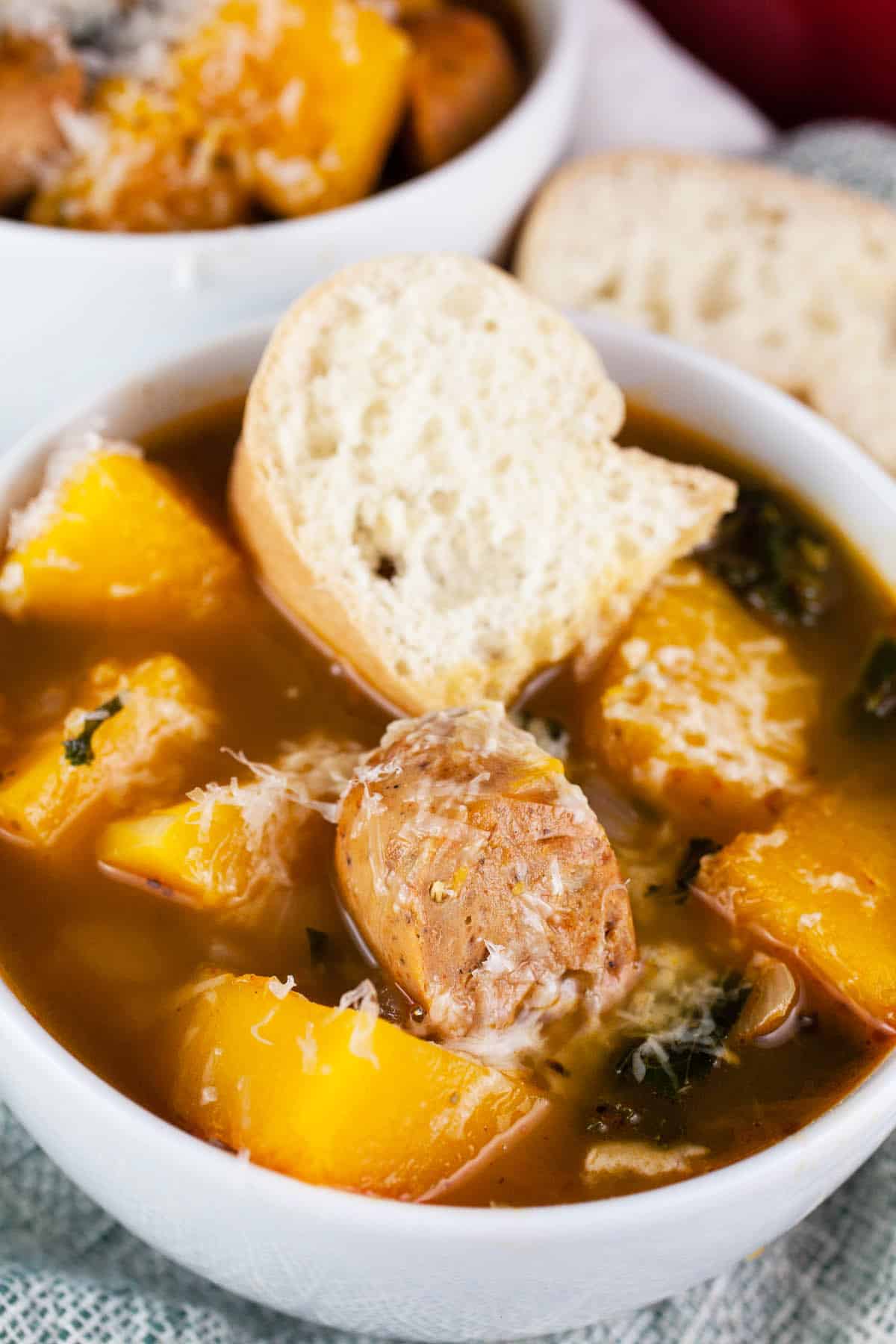 Squash and sausage soup in white bowl with slice of baguette bread.