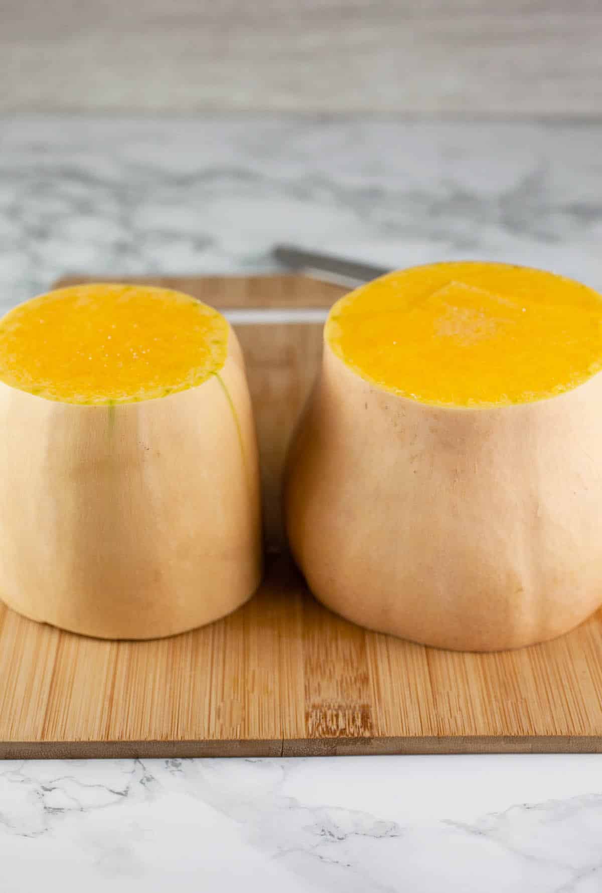 Butternut squash cut in half on wooden cutting board.