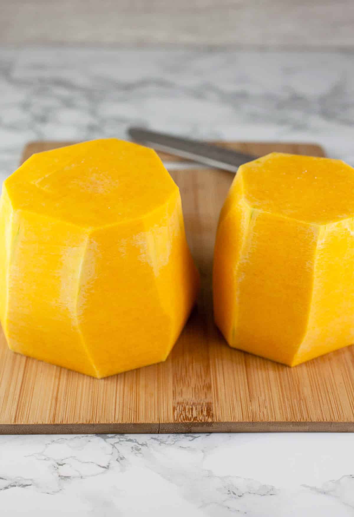 Peeled butternut squash halves on wooden cutting board.