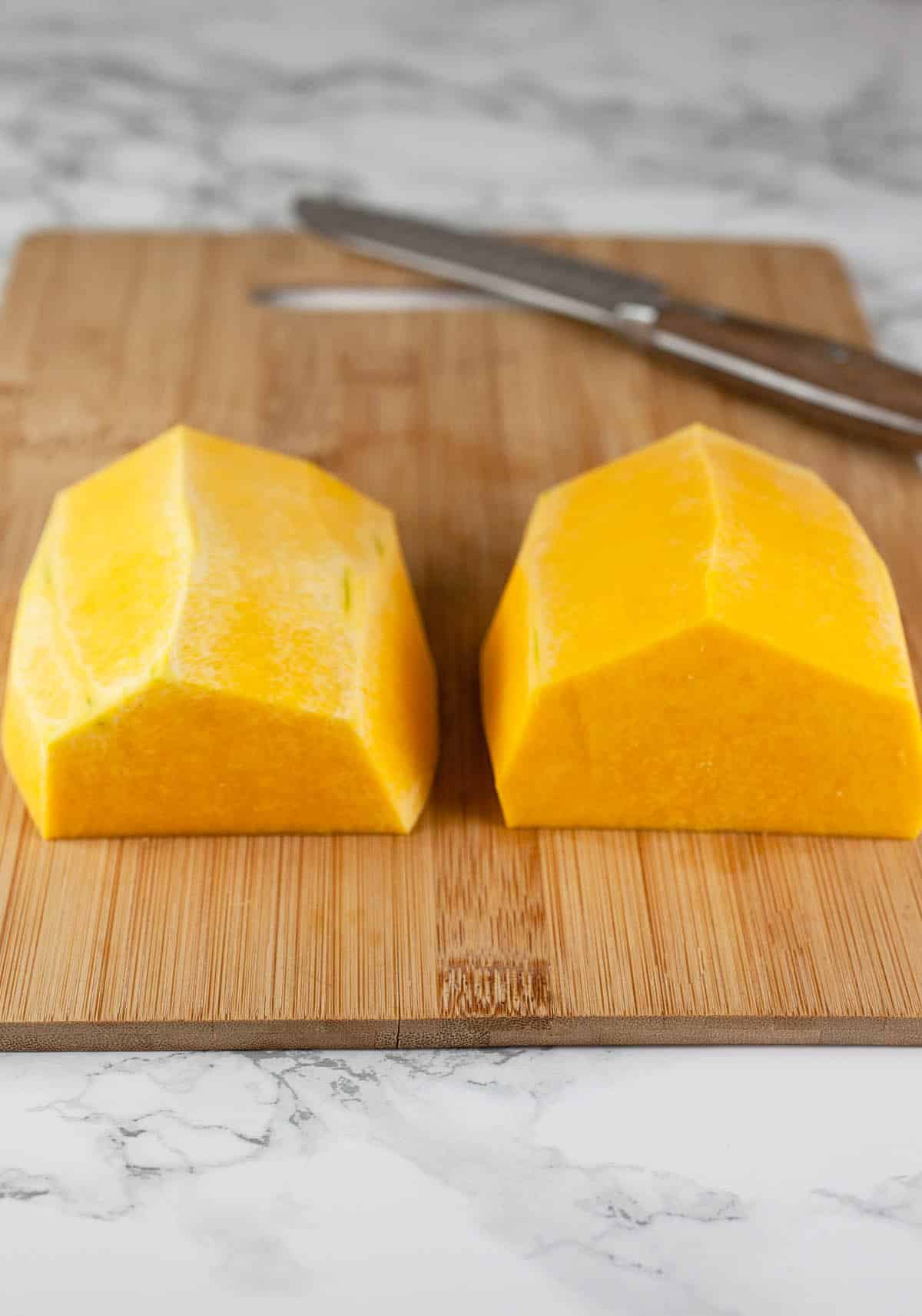 Peeled butternut squash half cut into halves on wooden cutting board.