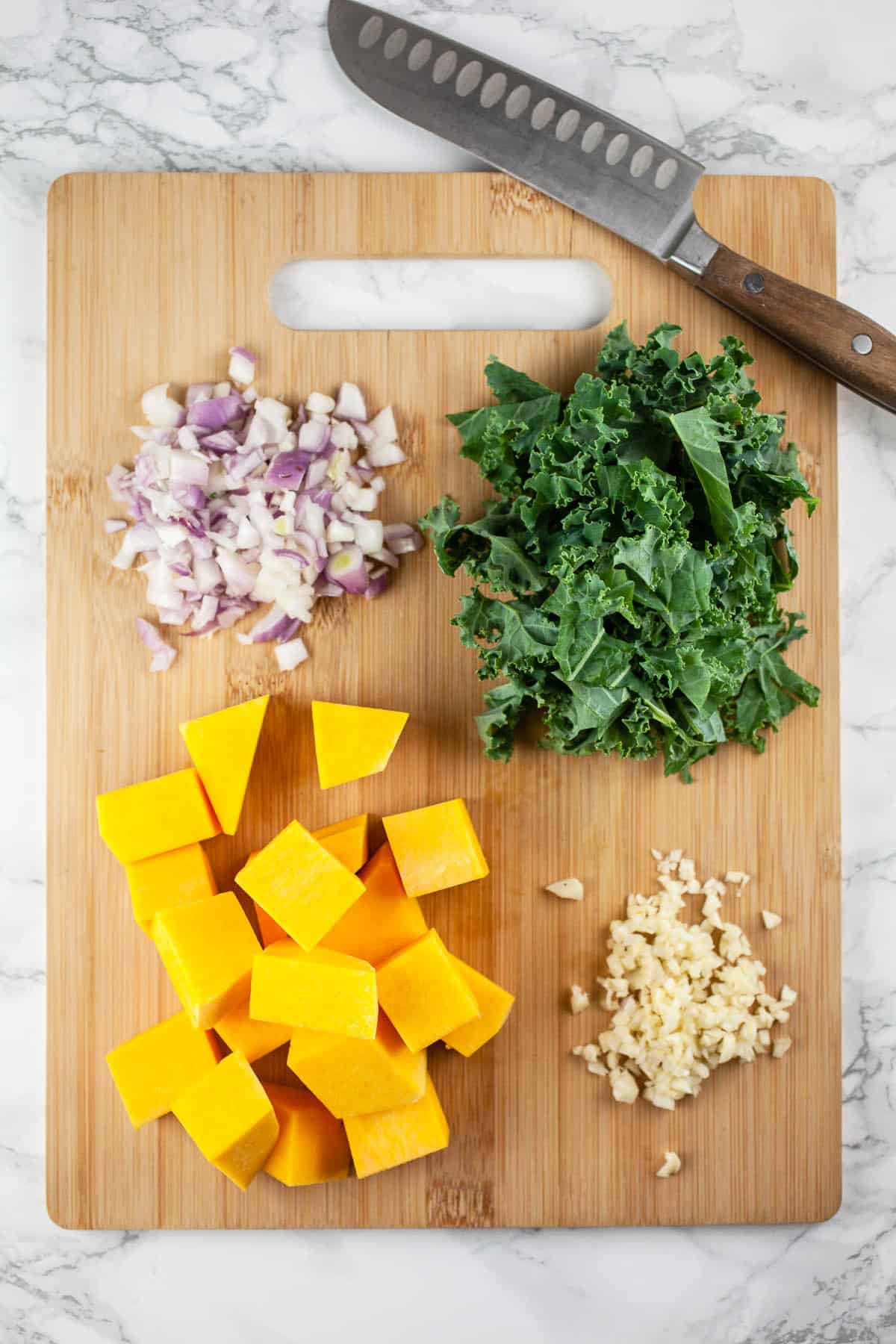 Squash chunks, minced garlic and onions, and chopped kale on wooden cutting board.