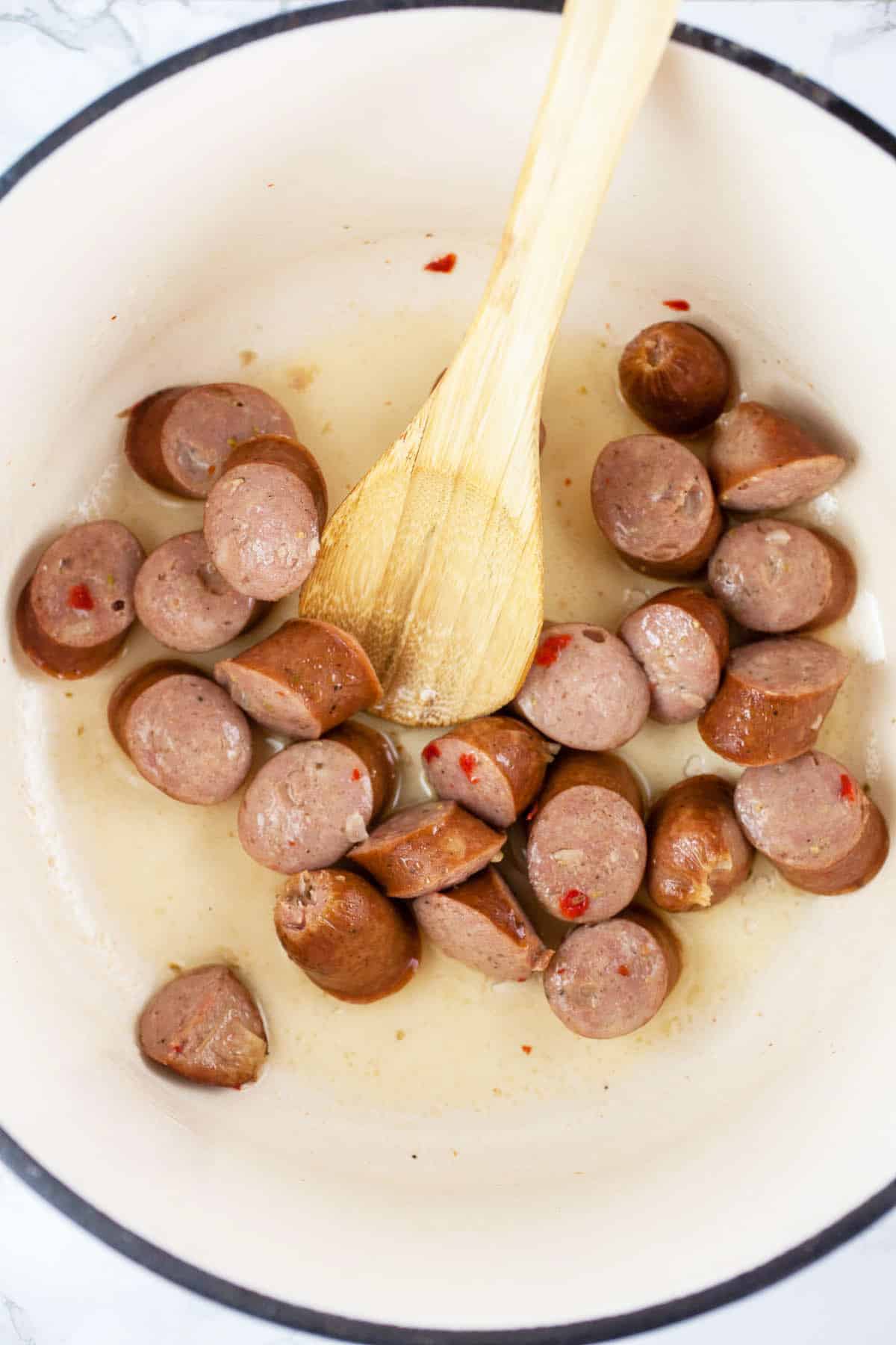 This Crockpot Butternut Squash and Sausage Soup is perfect for the cold winter months! It's hearty, healthy, and easy to make. This soup is made in the slow cooker. It's got chicken sausage, kale, and butternut squash. Soup is one of the best comfort foods out there! I love hearty soup recipes like this. #soup #crockpot #slowcooker #butternutsquash #sausage #kale Chicken sausage sautéed in Dutch oven with wooden spoon.