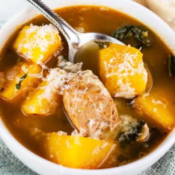Butternut squash sausage kale soup in white bowl with spoon.