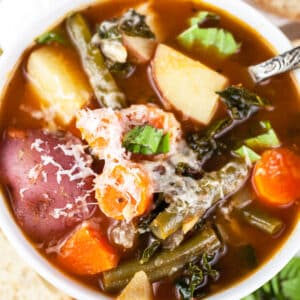 Italian chunky vegetable soup with Parmesan cheese in small white bowl.